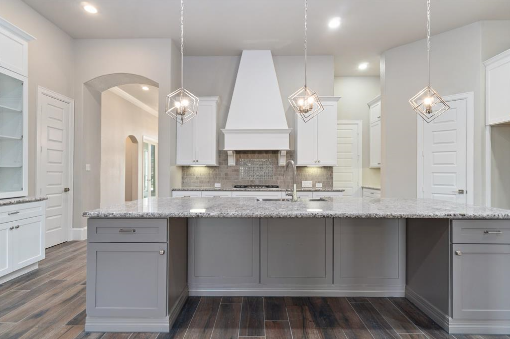 Modern kitchen with a large island, granite countertops, pendant lighting, gray cabinets, and wood flooring.