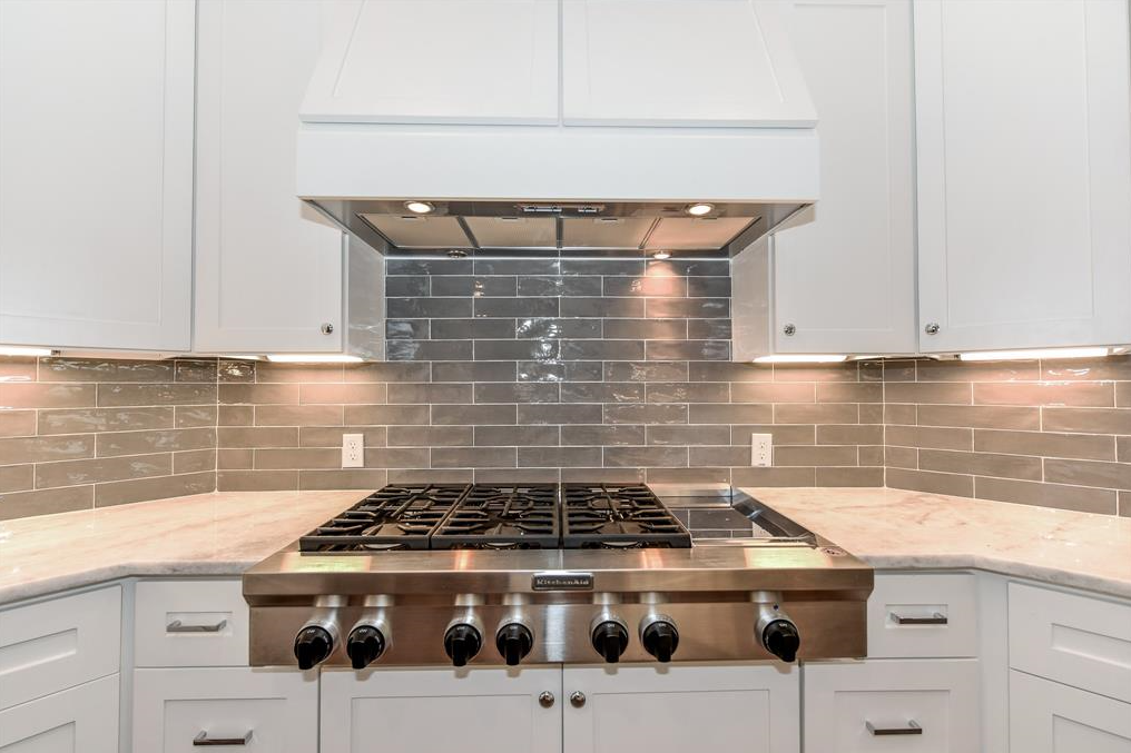 Modern kitchen with stainless steel gas stove, white cabinets, and gray tile backsplash.