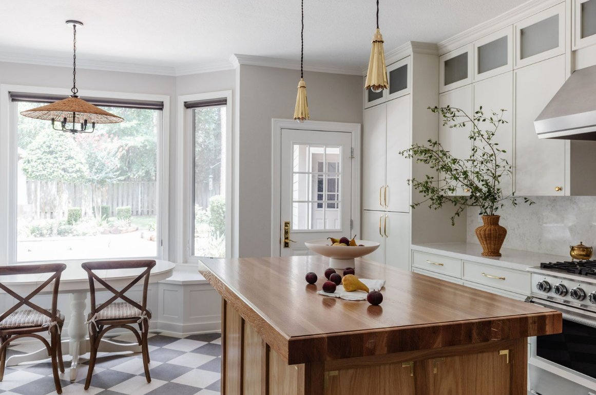 Modern kitchen with wooden island, fruit bowl, potted plant, stove, pendant lights, and large windows.