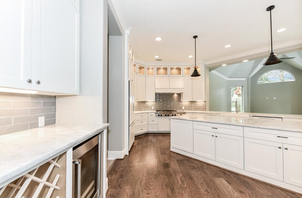 Modern kitchen with white cabinets, marble countertops, dark wood flooring, a stainless steel oven, two pendant lights, and gray tile backsplash.