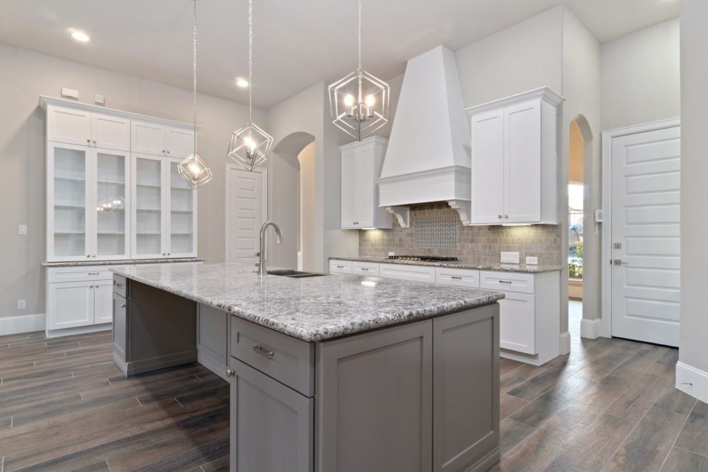 Modern kitchen with gray cabinets, marble countertops, wood flooring, pendant lights, and a large kitchen island.