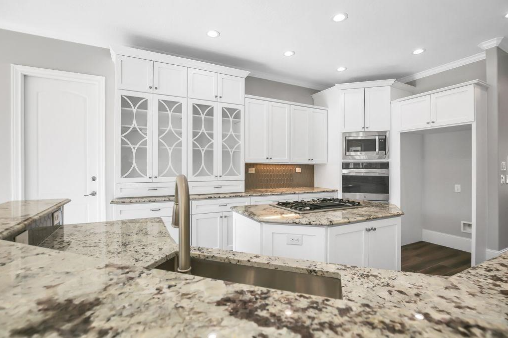 Modern kitchen with white cabinets, marble countertops, and stainless steel appliances. Features an island with a built-in cooktop and a sink with a modern faucet.