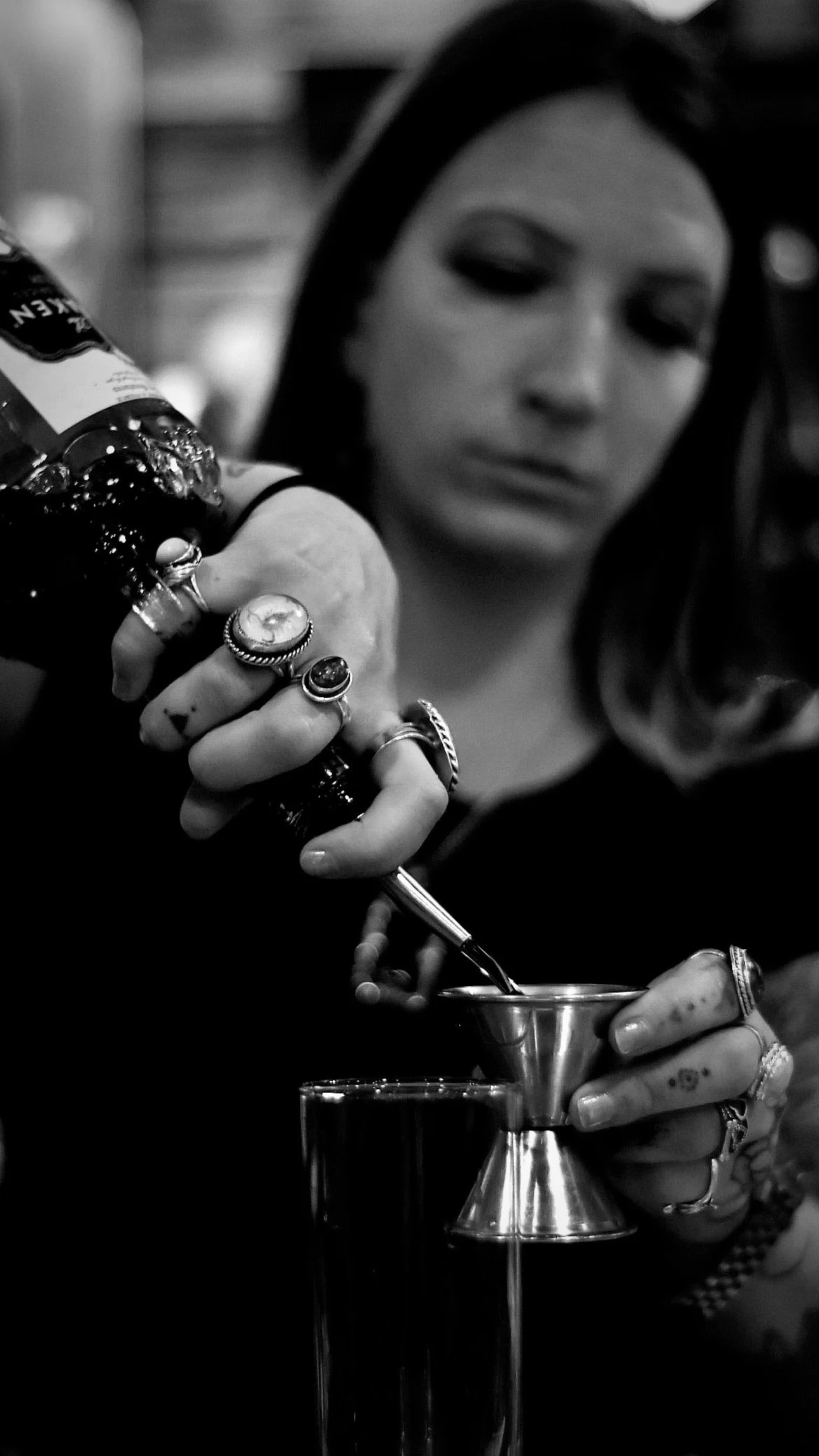 Woman pouring liquid into a jigger with various rings on her fingers
