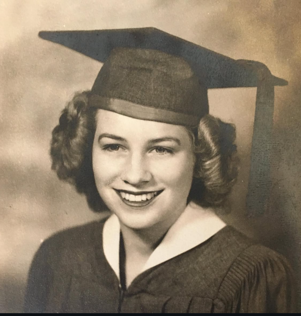Black and white photo of a smiling young woman in a graduation cap and gown.