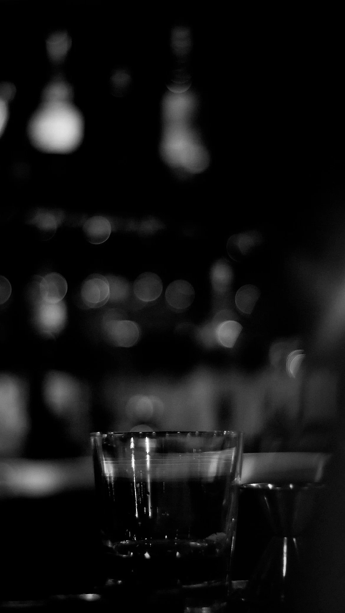 A glass of water and a small metal cup on a surface with a blurred cityscape background with lights.