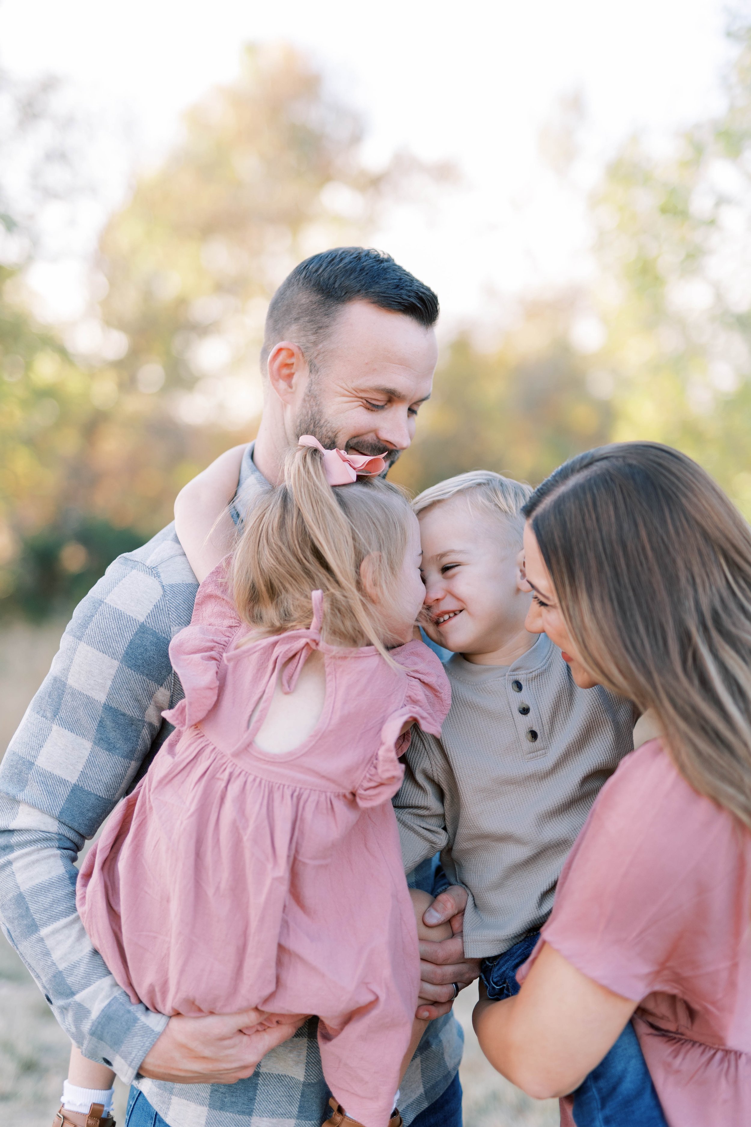 A happy family of four, a father, mother, son, and daughter, sharing a close, affectionate moment outdoors during the daytime. Family photography in Medford, Oregon.