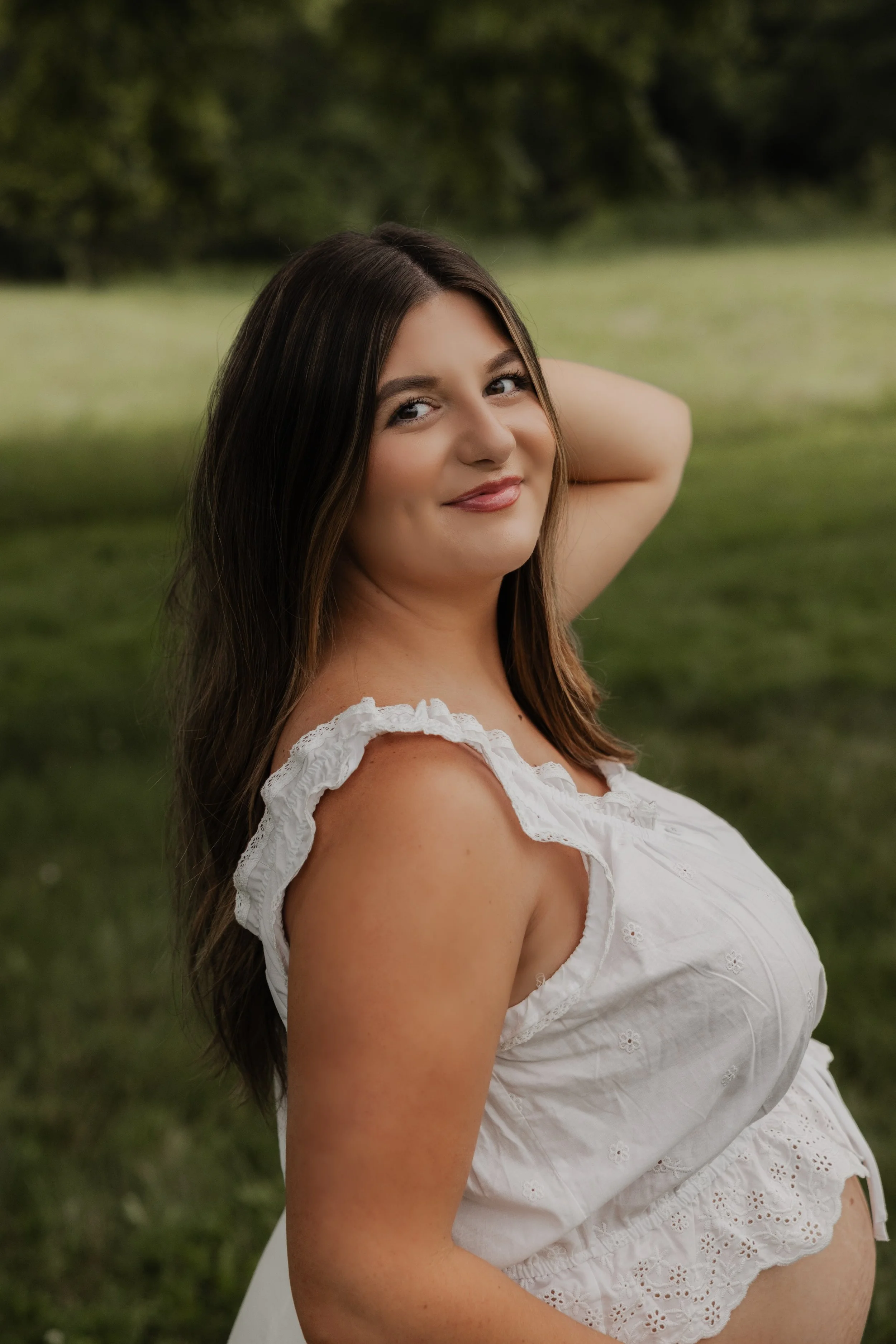 A woman sitting on the floor, wearing a white blouse and blue jeans, with long hair and a smile, posing against a plain background.