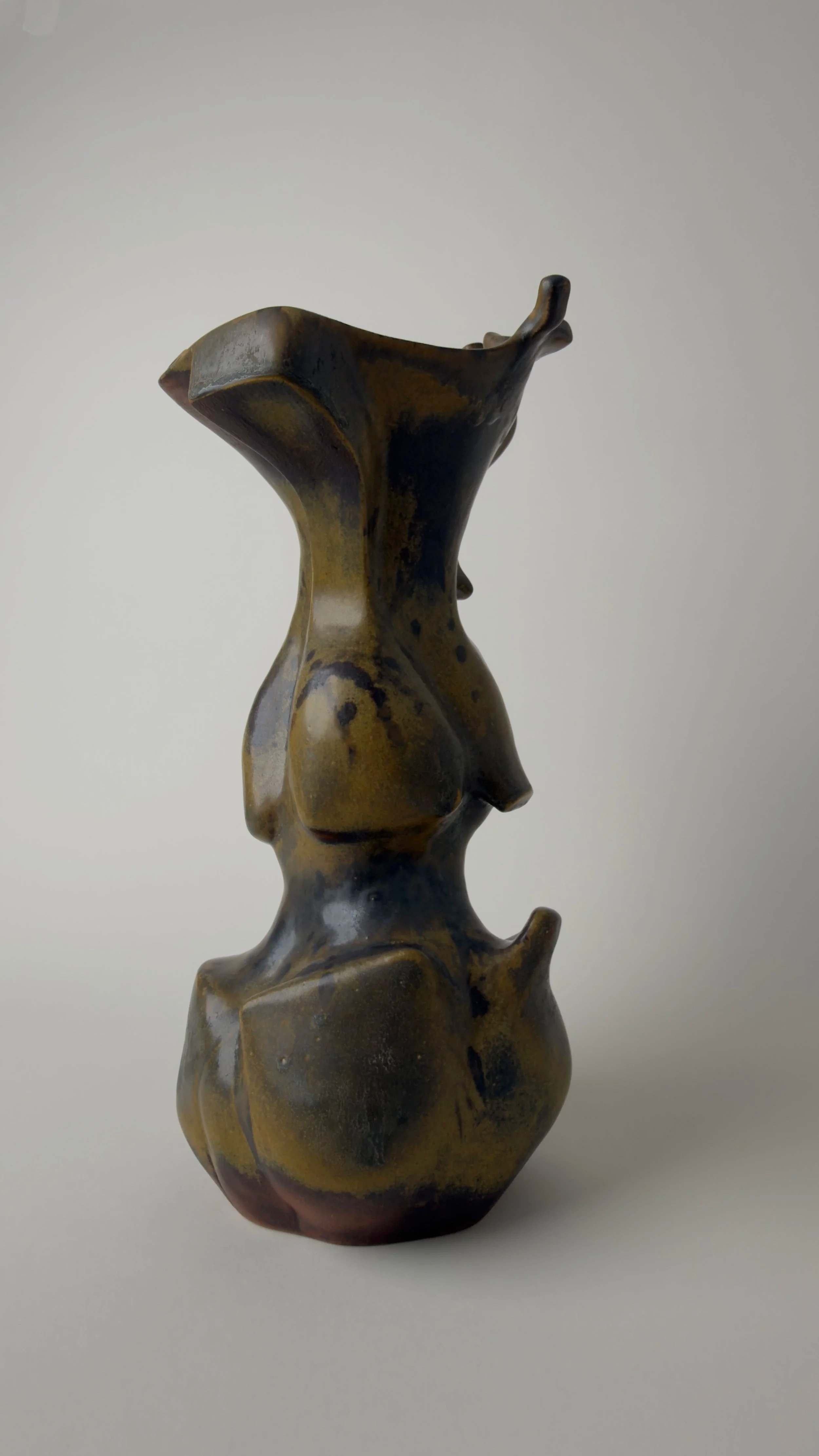 Sculptural ceramic vessel with an elongated organic form, branching openings and a dark bronze and black glazed surface.