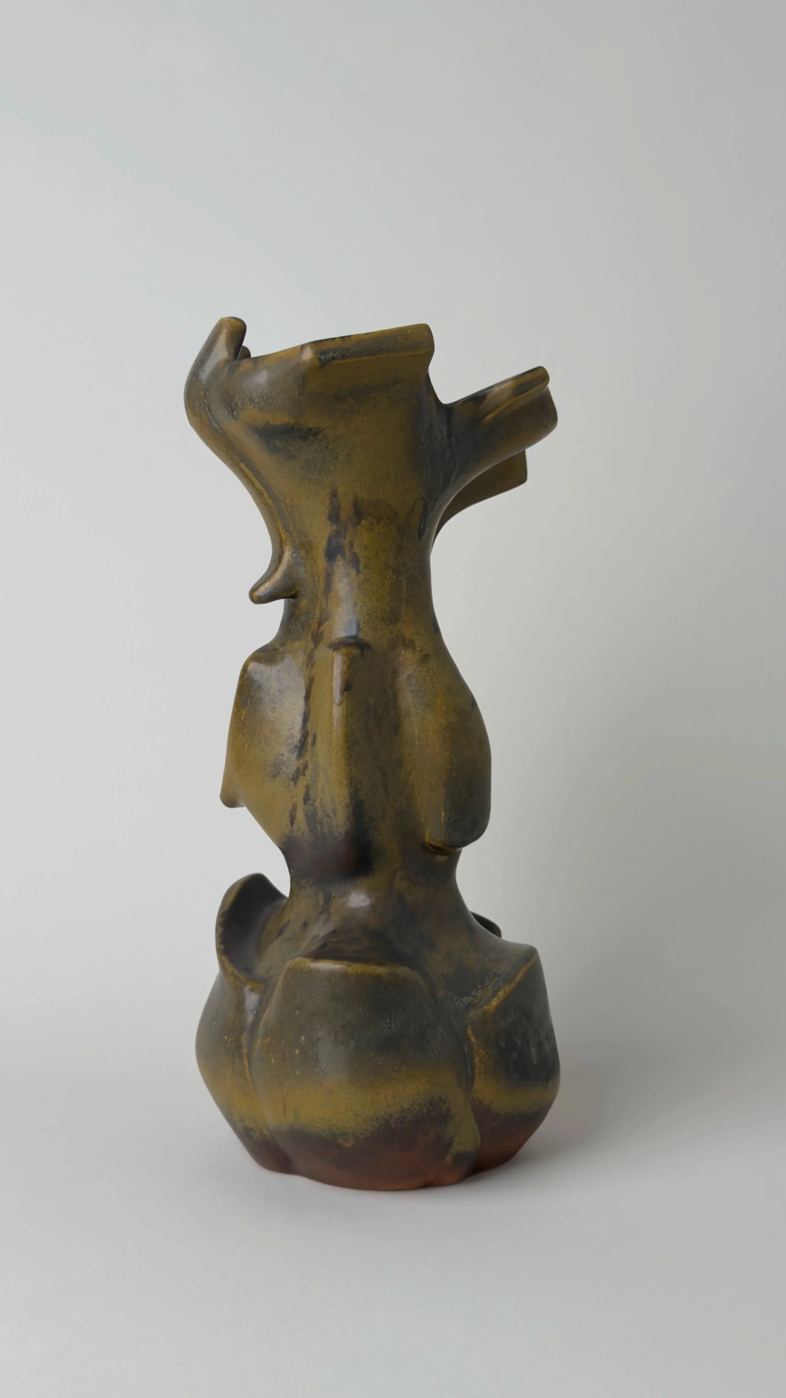 Sculptural ceramic vessel with an elongated organic form, branching openings and a dark bronze and black glazed surface.