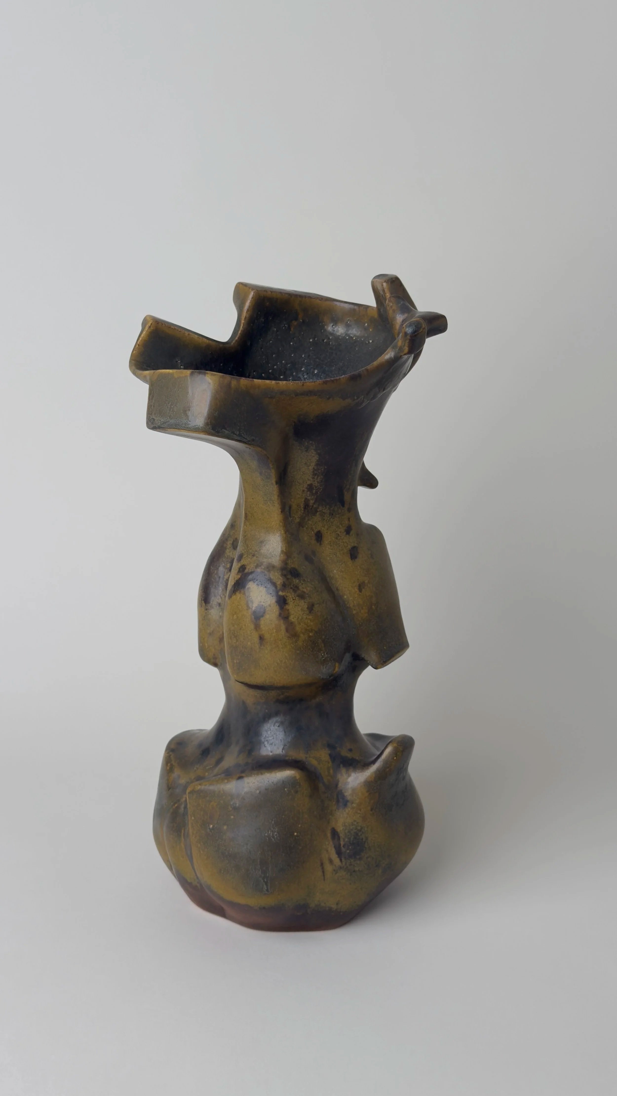 Sculptural ceramic vessel with an elongated organic form, branching openings and a dark bronze and black glazed surface.