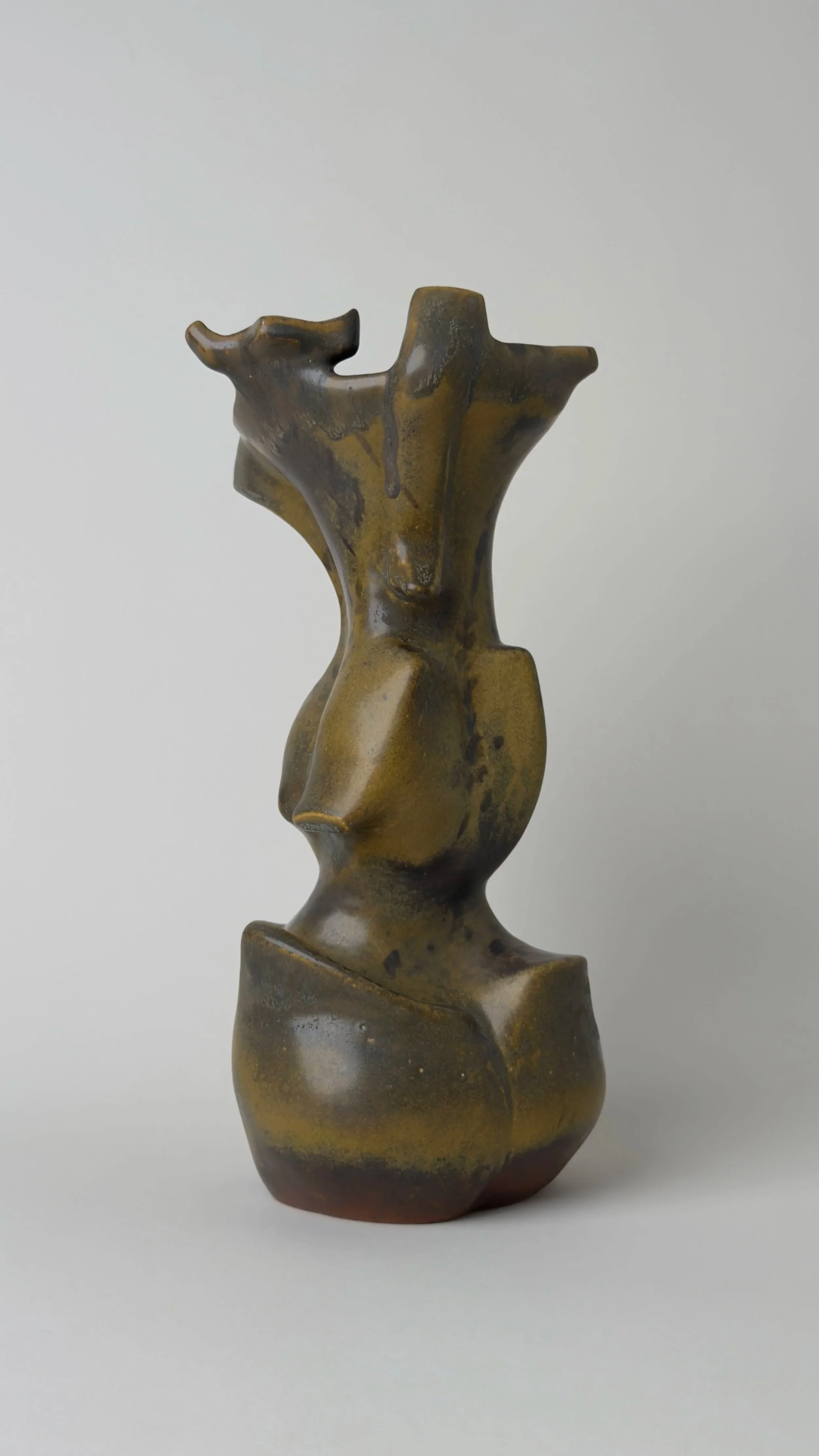 Abstract sculpture of a stylized human torso with emphasis on the chest and hips, made of a bronze-like material with a patina finish.