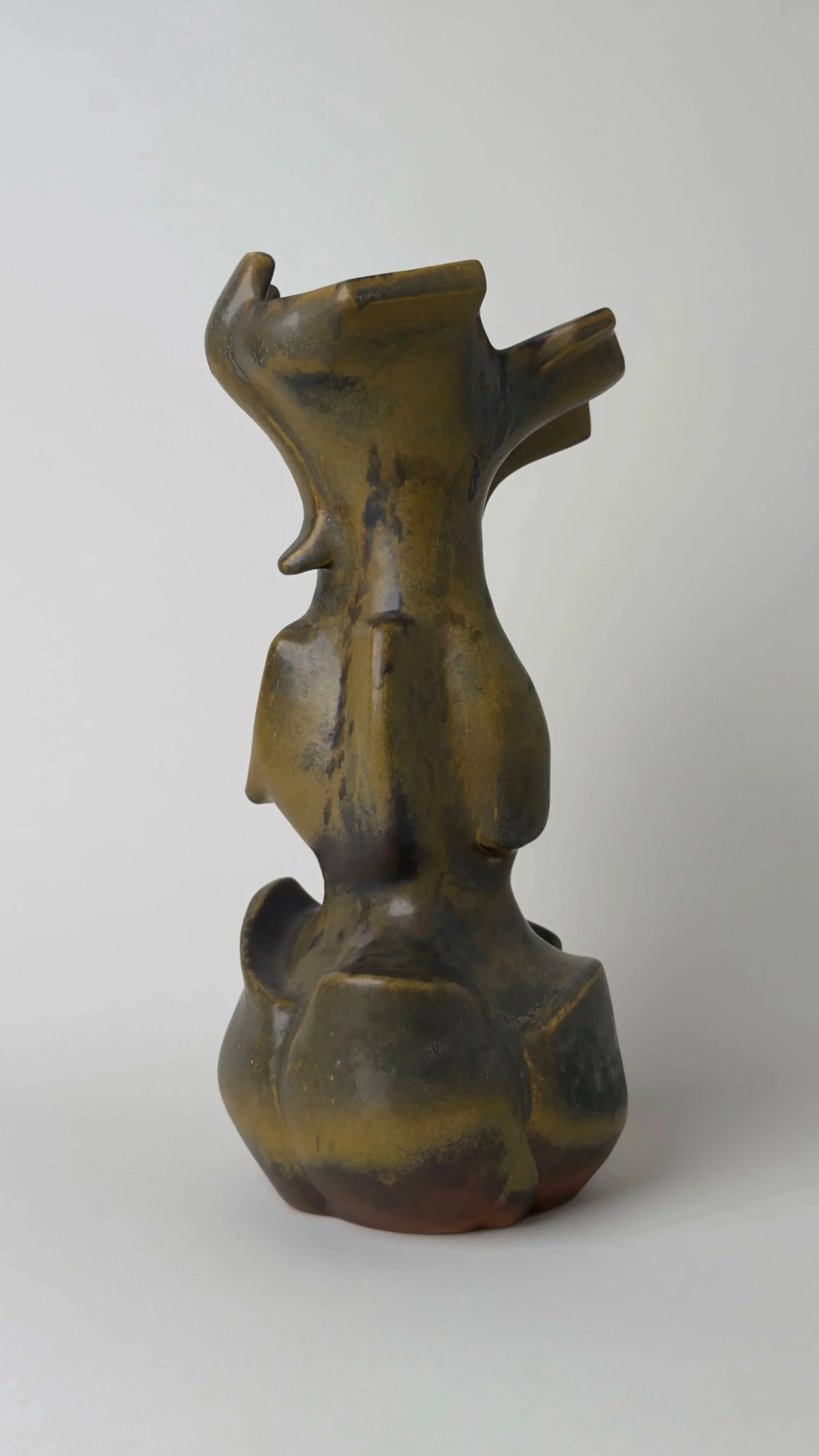 Sculptural ceramic vessel with an elongated organic form, branching openings and a dark bronze and black glazed surface.