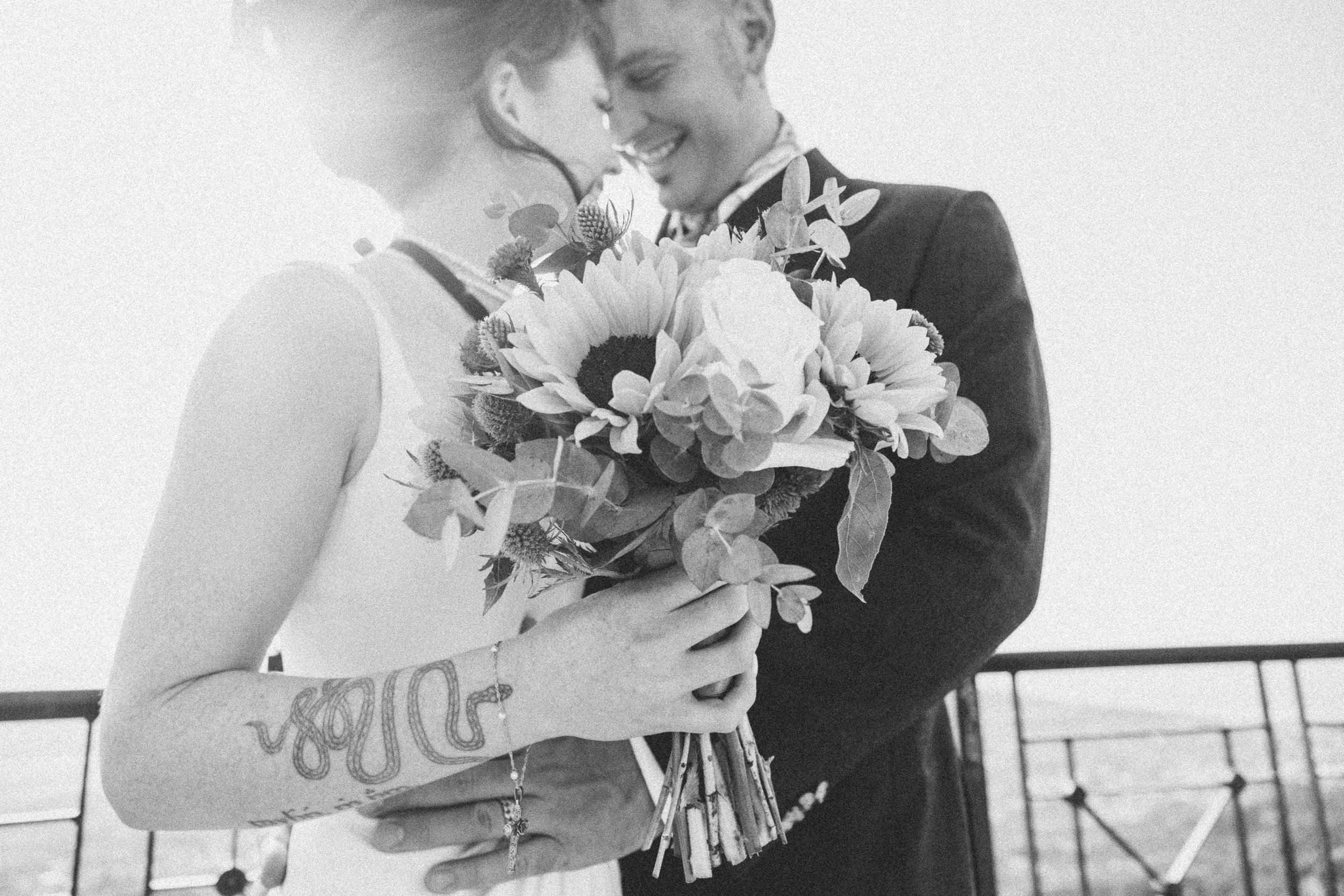 Black and white photo of a bride and groom sharing a moment, with the bride holding a bouquet of flowers.