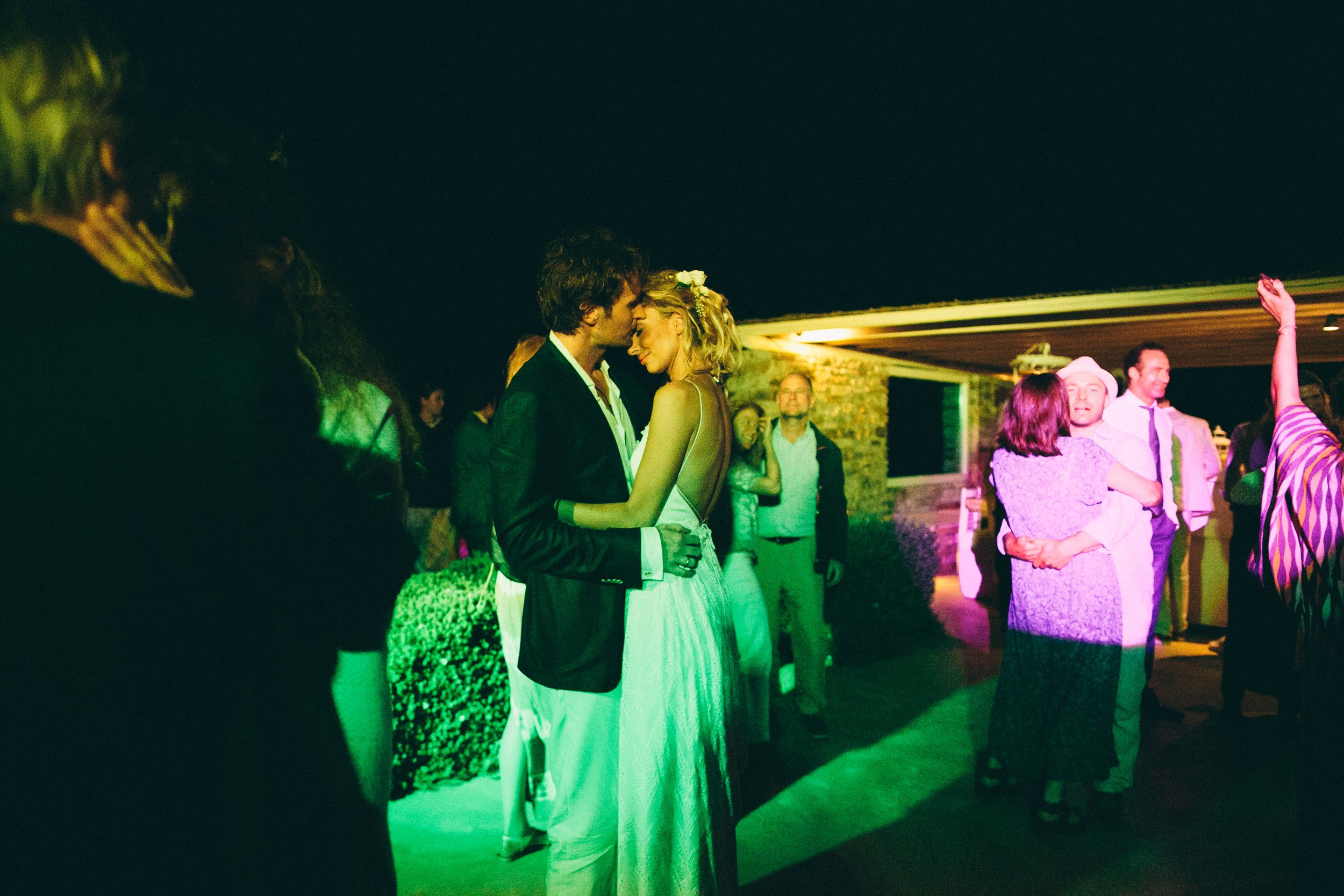 Couple embracing and dancing at a nighttime outdoor party with other guests in the background.
