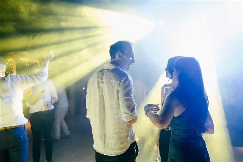 People dancing and socializing at an indoor party with yellow and white lighting.