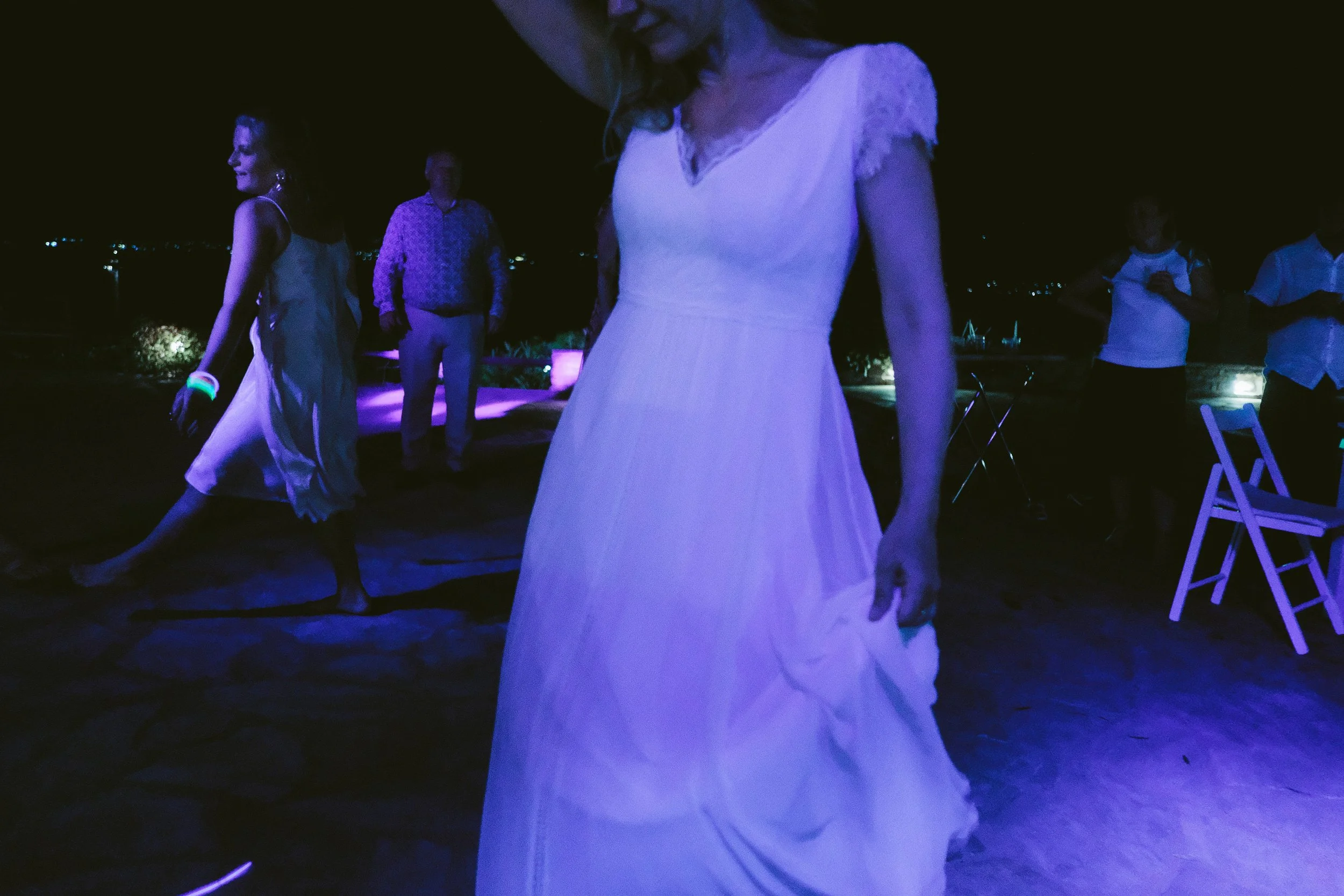 People dancing at night, with a woman in the foreground wearing a white dress, on a dark outdoor dance floor.