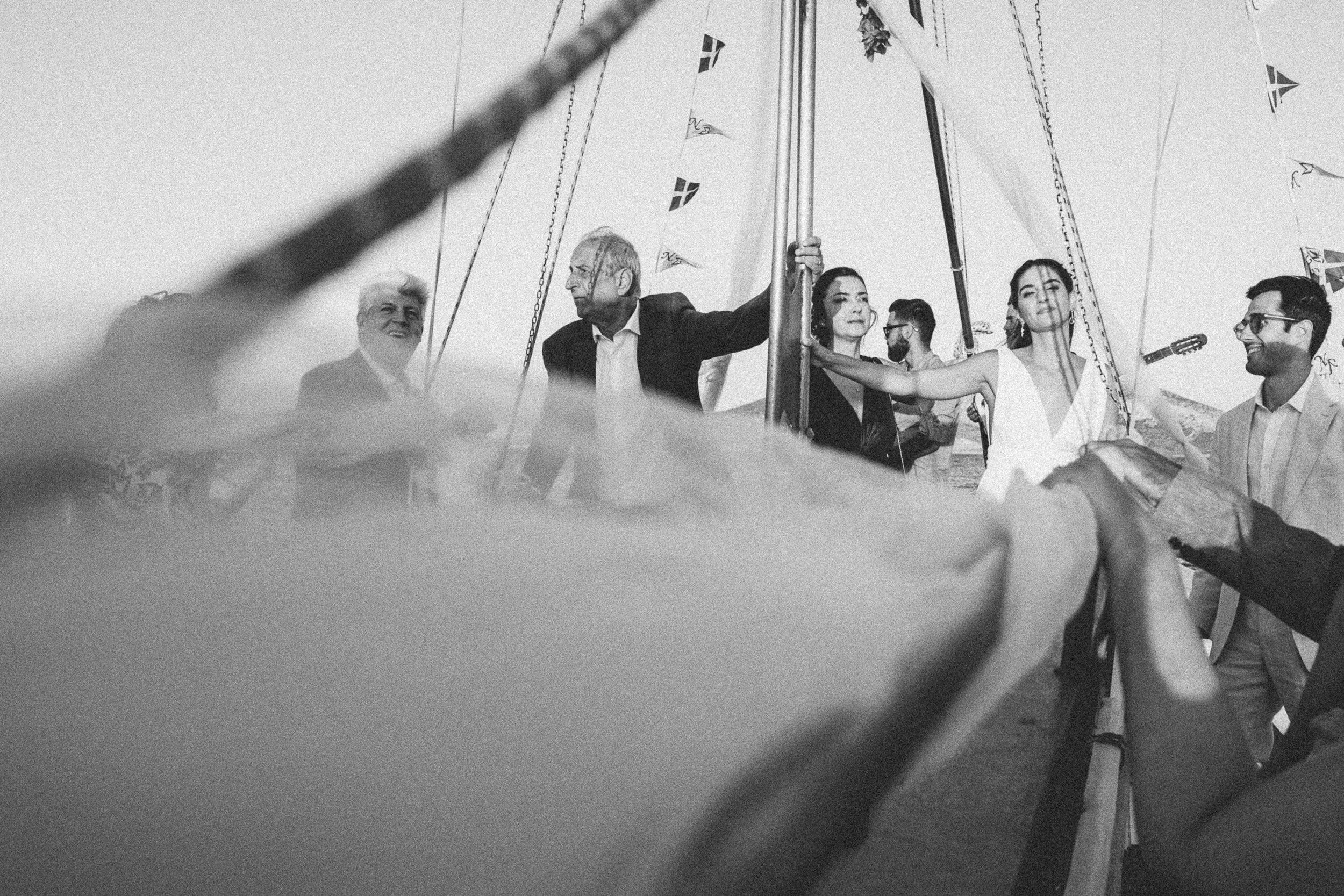 A group of people on a boat holding a flag, with some smiling and others looking serious, in black and white.