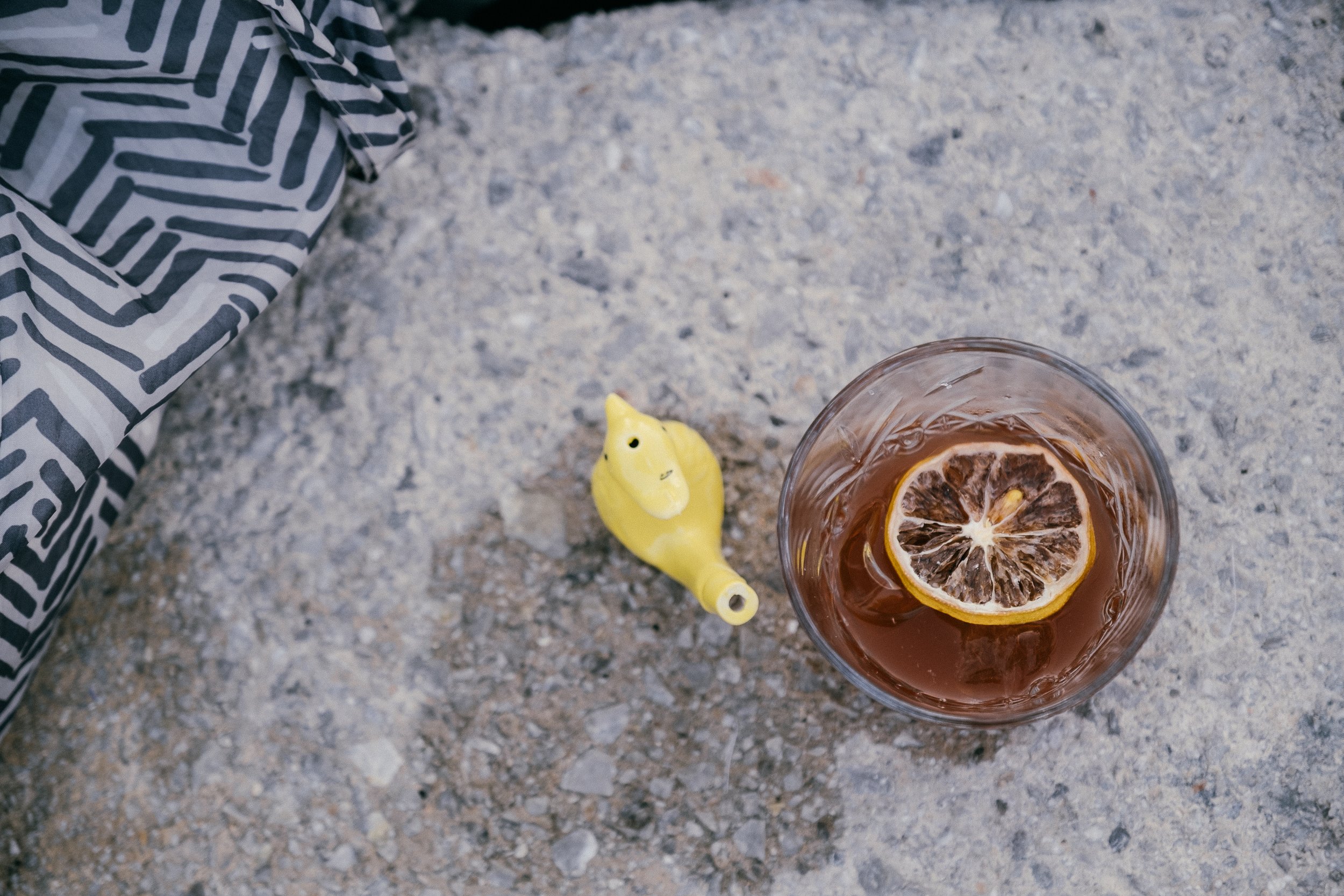 A glass of iced tea with a lemon slice, a yellow bath bomb shaped like a duck, and part of a patterned fabric on a textured surface.