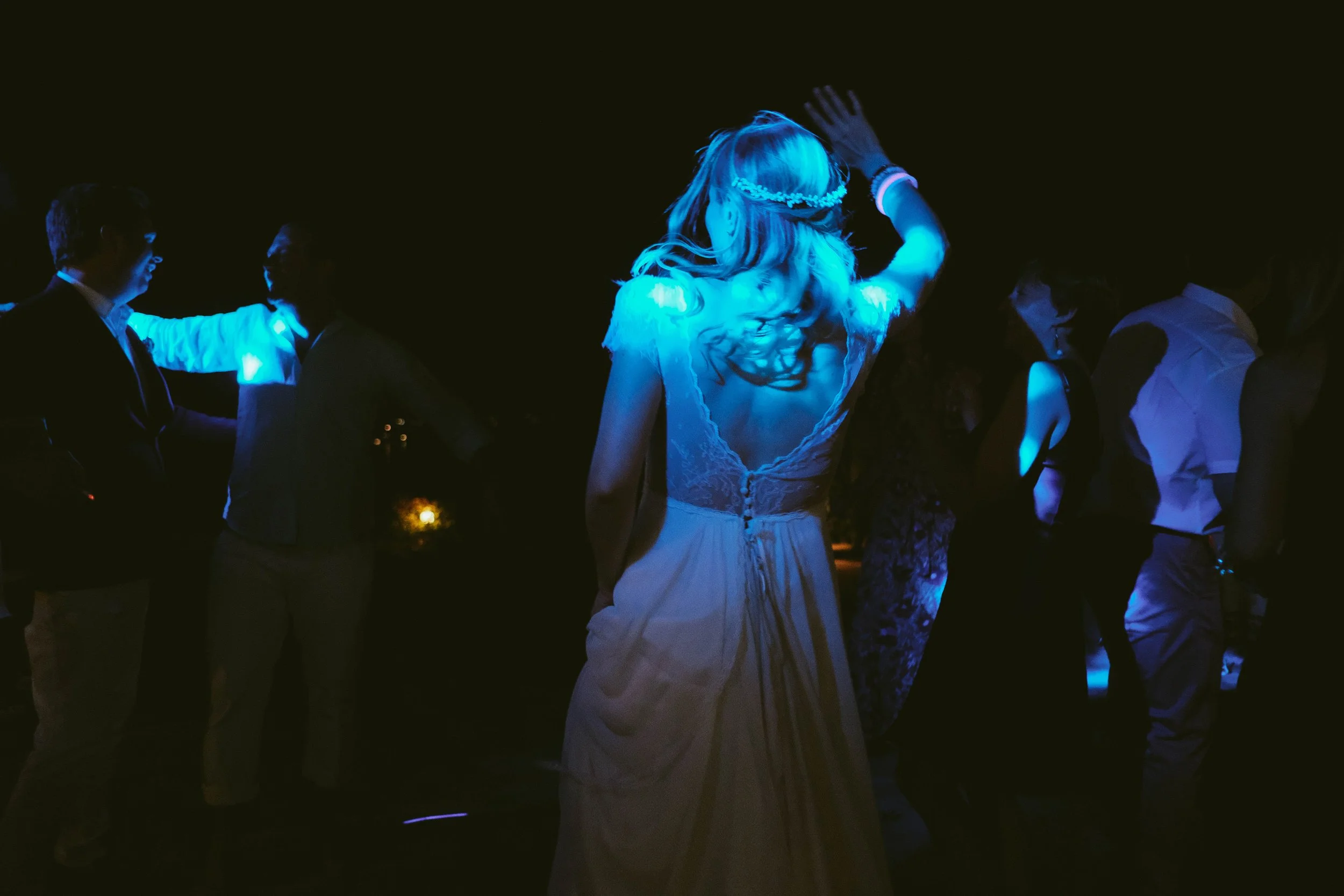 People dancing at a party or celebration in a dark setting with blue lighting.
