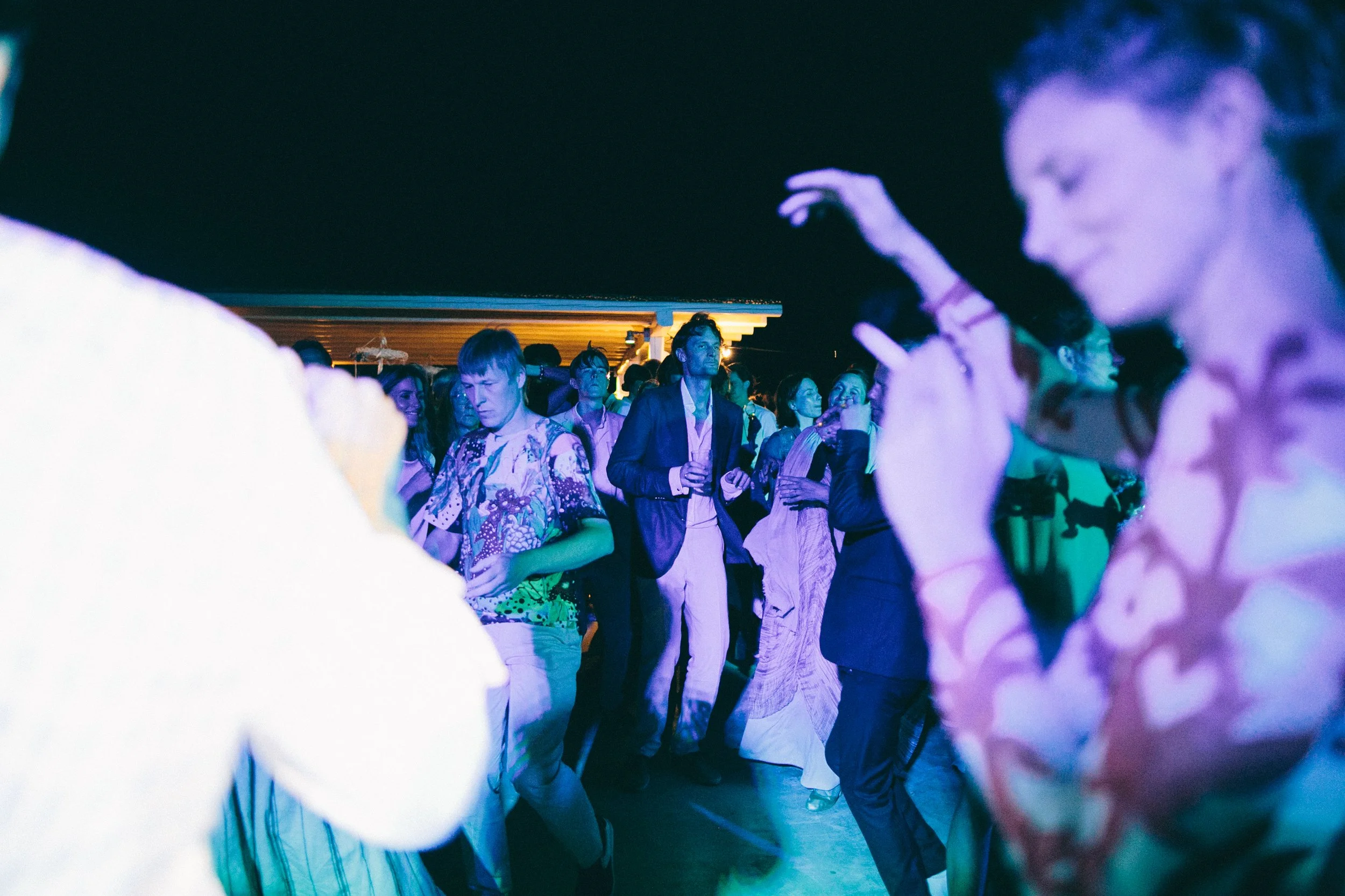 People dancing at a party under colorful lights on a rooftop at night.