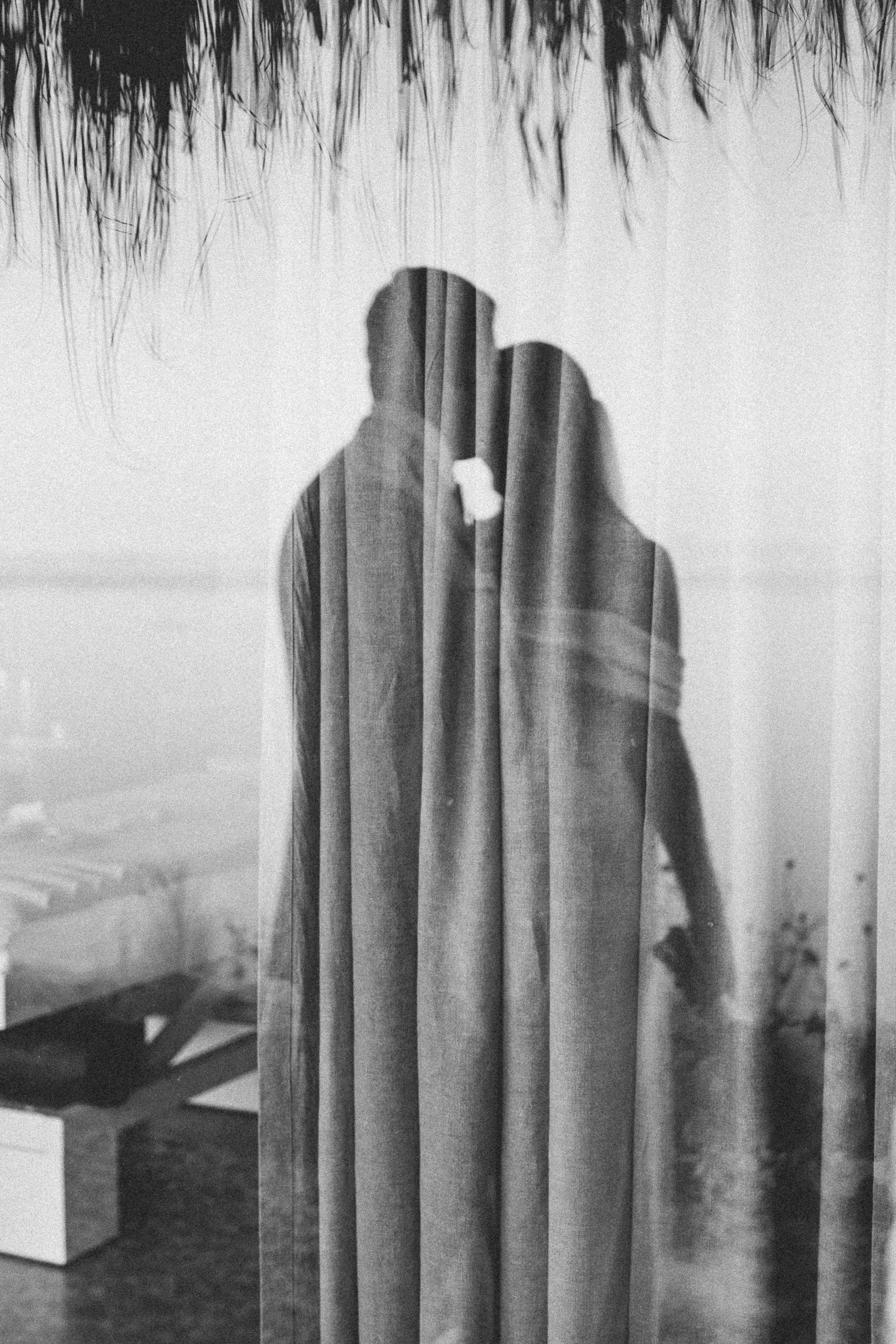 A reflection of a couple kissing behind a curtain, creating a layered, artistic image.