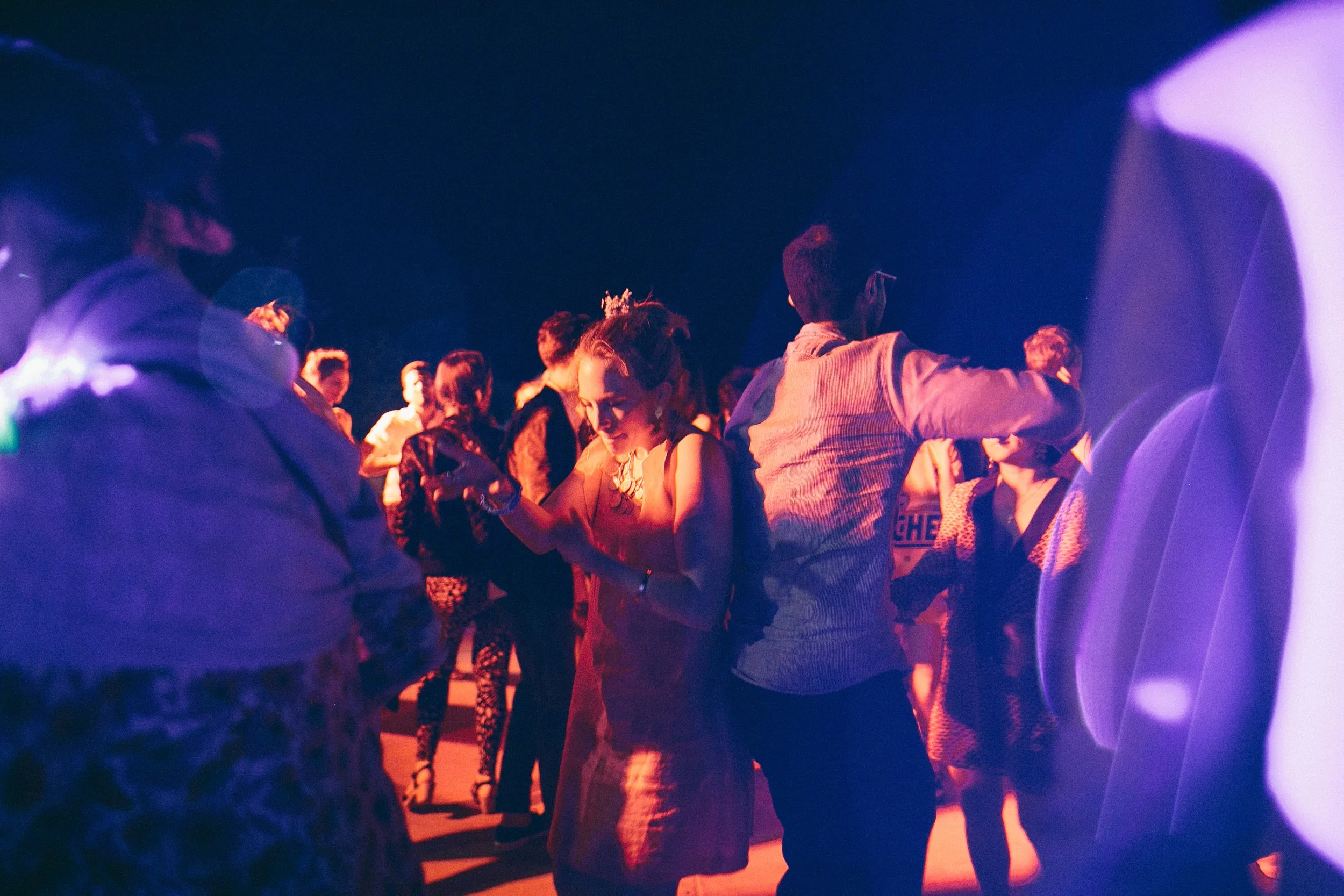 People dancing at a party or nightclub with colorful, dim lighting.