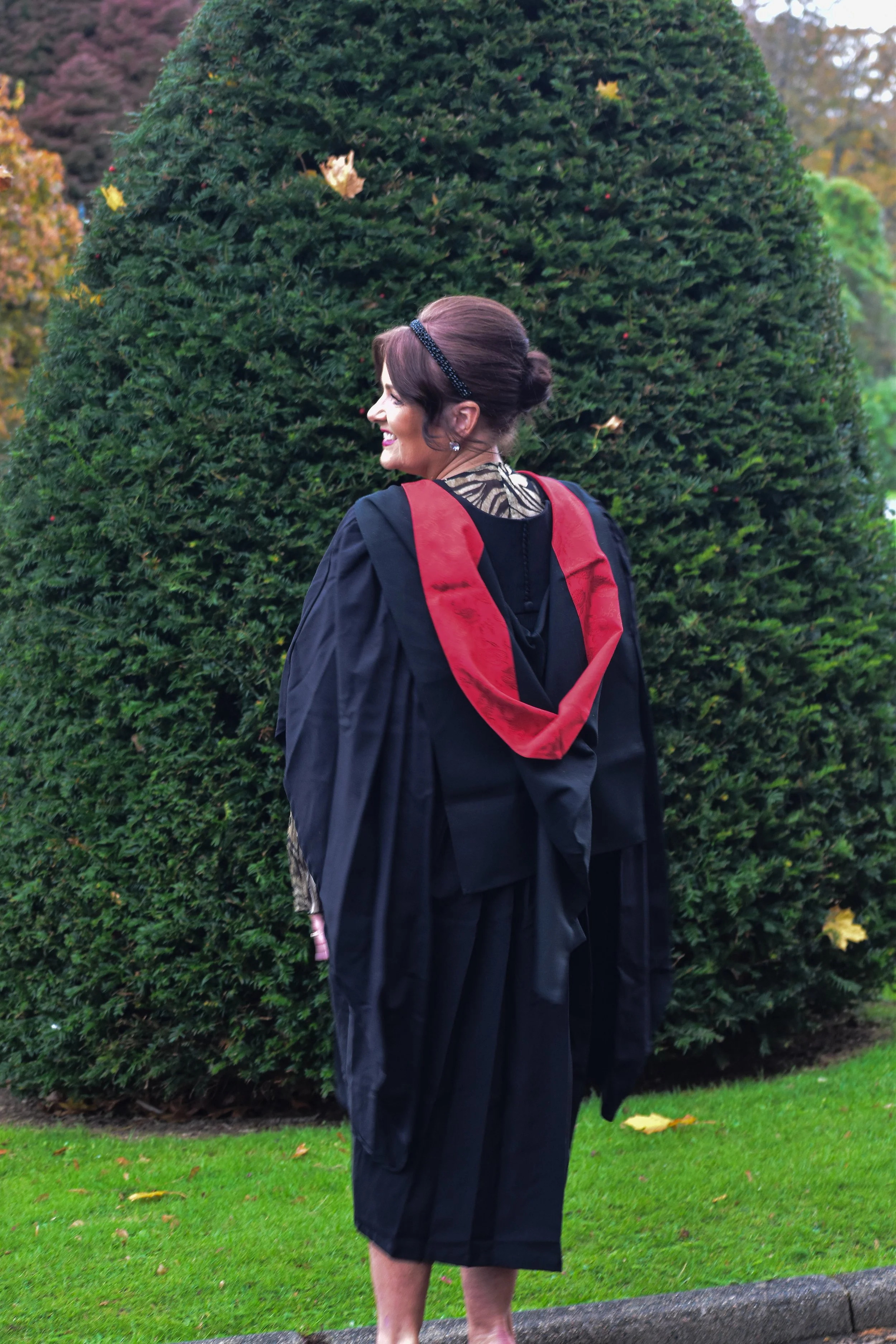 Woman in graduation gown with red hood standing outdoors