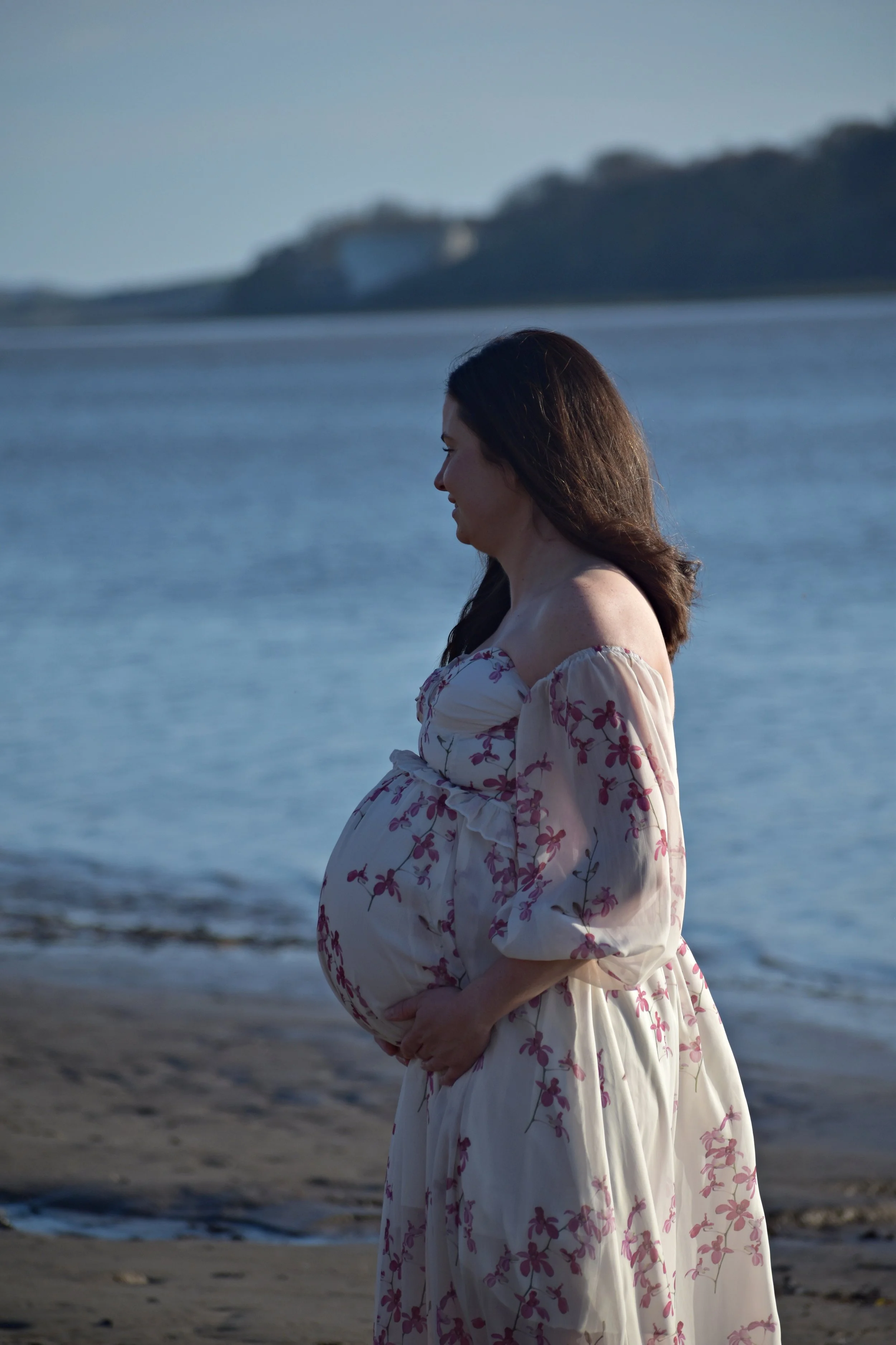 Pregnant woman in floral dress standing on a beach