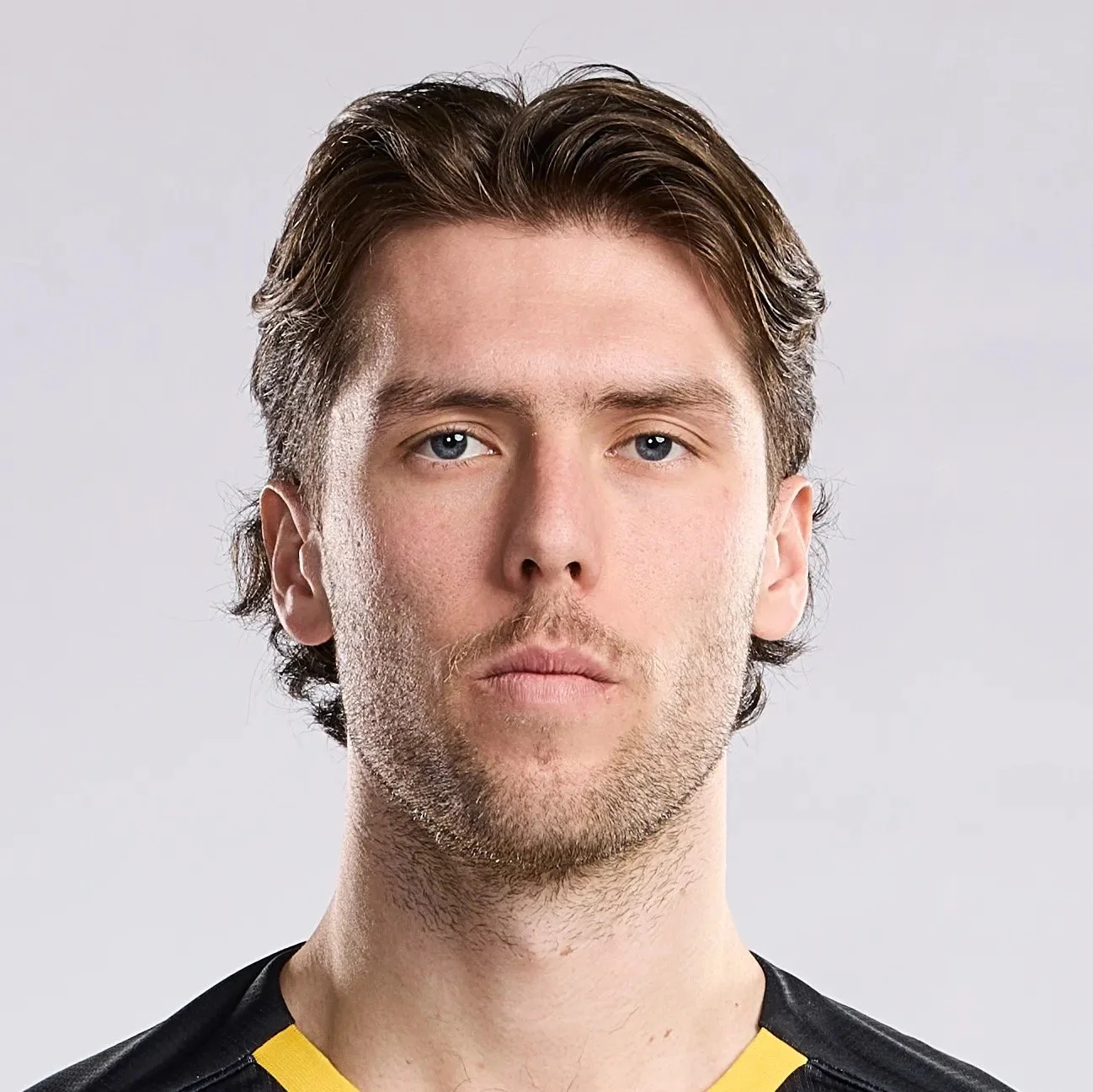 Bradley Sample. Bubble Dudes. Pittsburgh Riverhounds. Soccer. Clean. Close-up of a young man with light skin, light brown hair, and blue eyes, wearing a black shirt with yellow accents, looking directly at the camera against a plain light background.