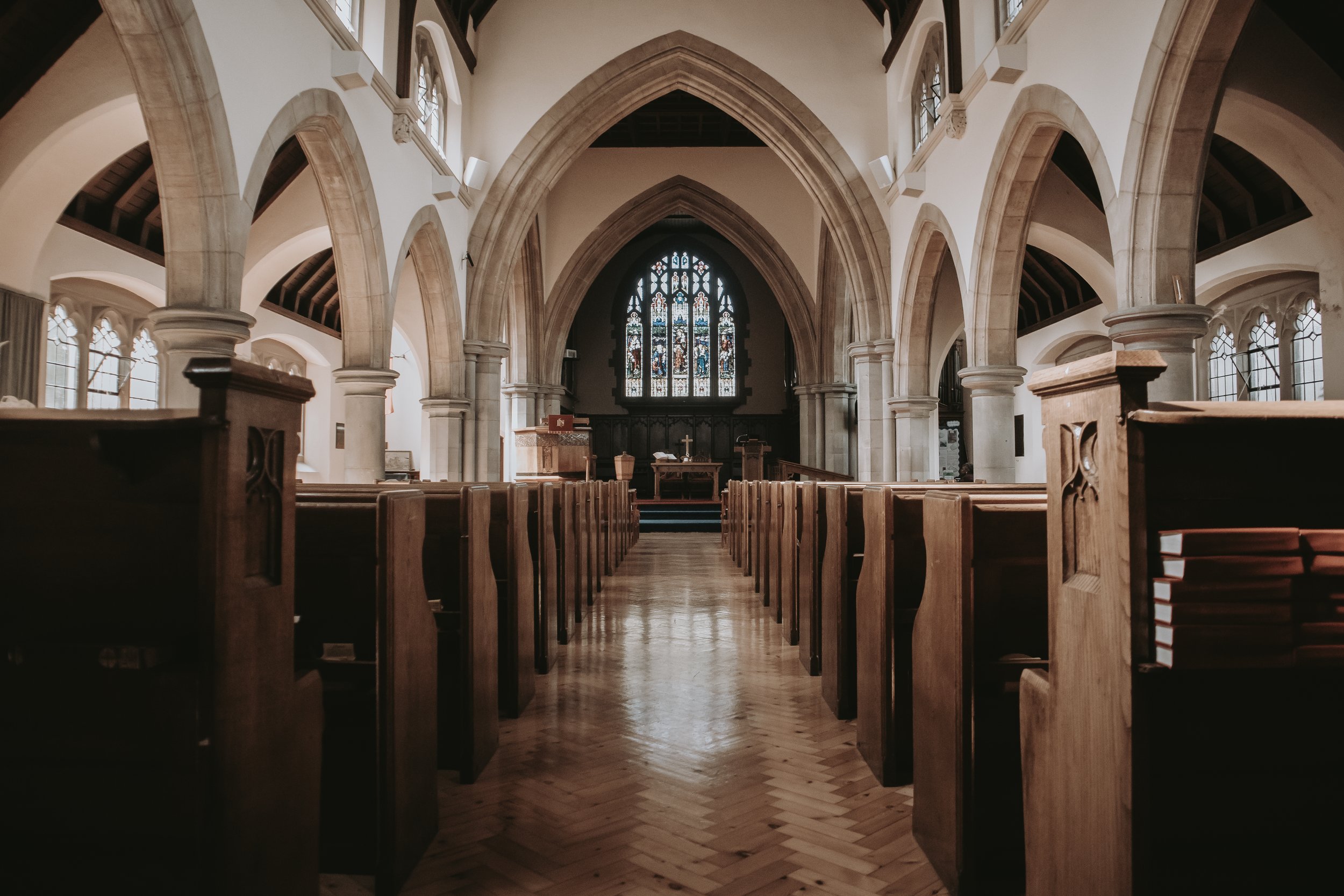 Interior of a church with wooden pews, arched ceilings, and stained glass window.