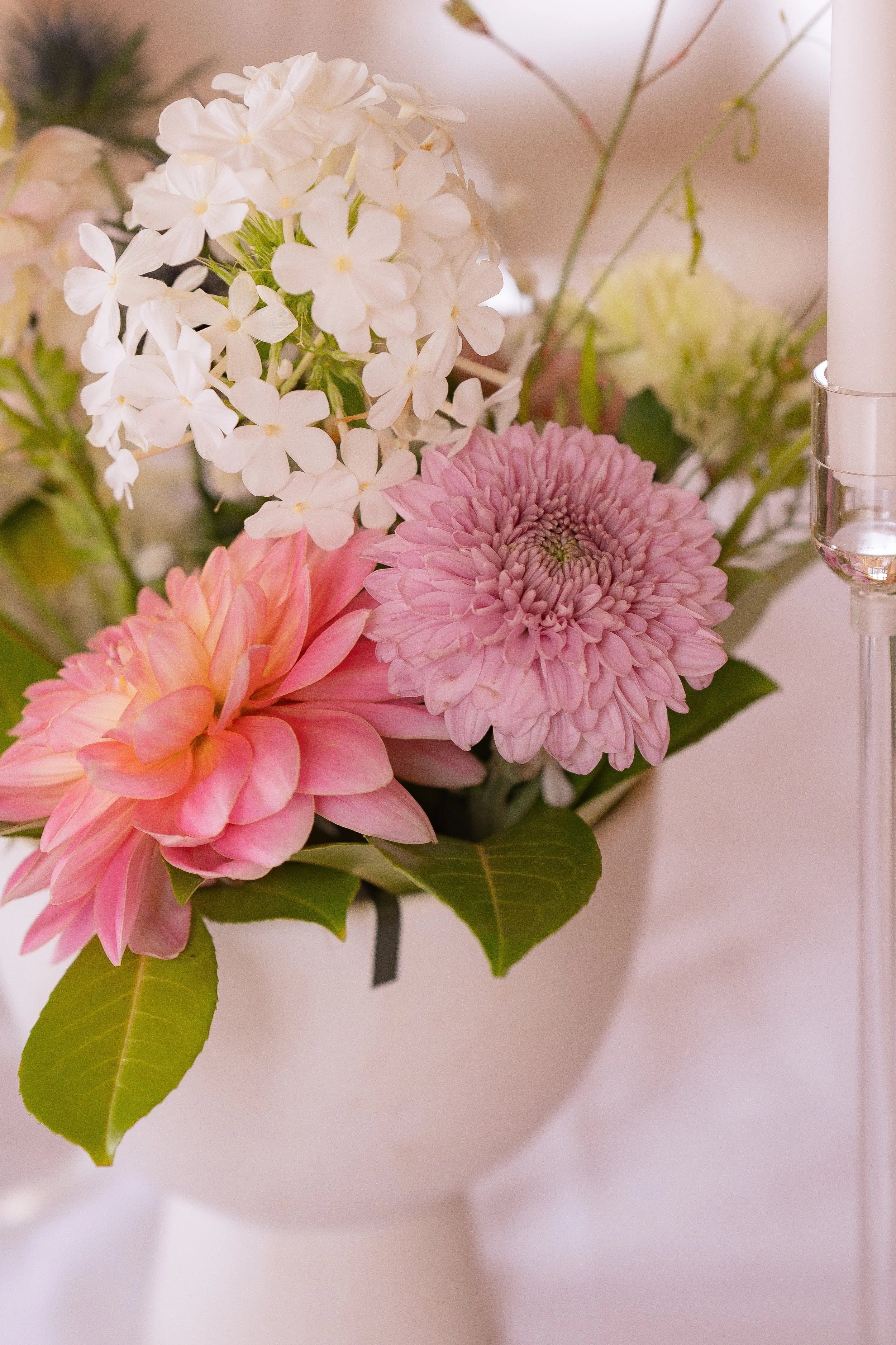 A white vase holding a floral arrangement with pink dahlias, white hydrangeas, and assorted greenery.