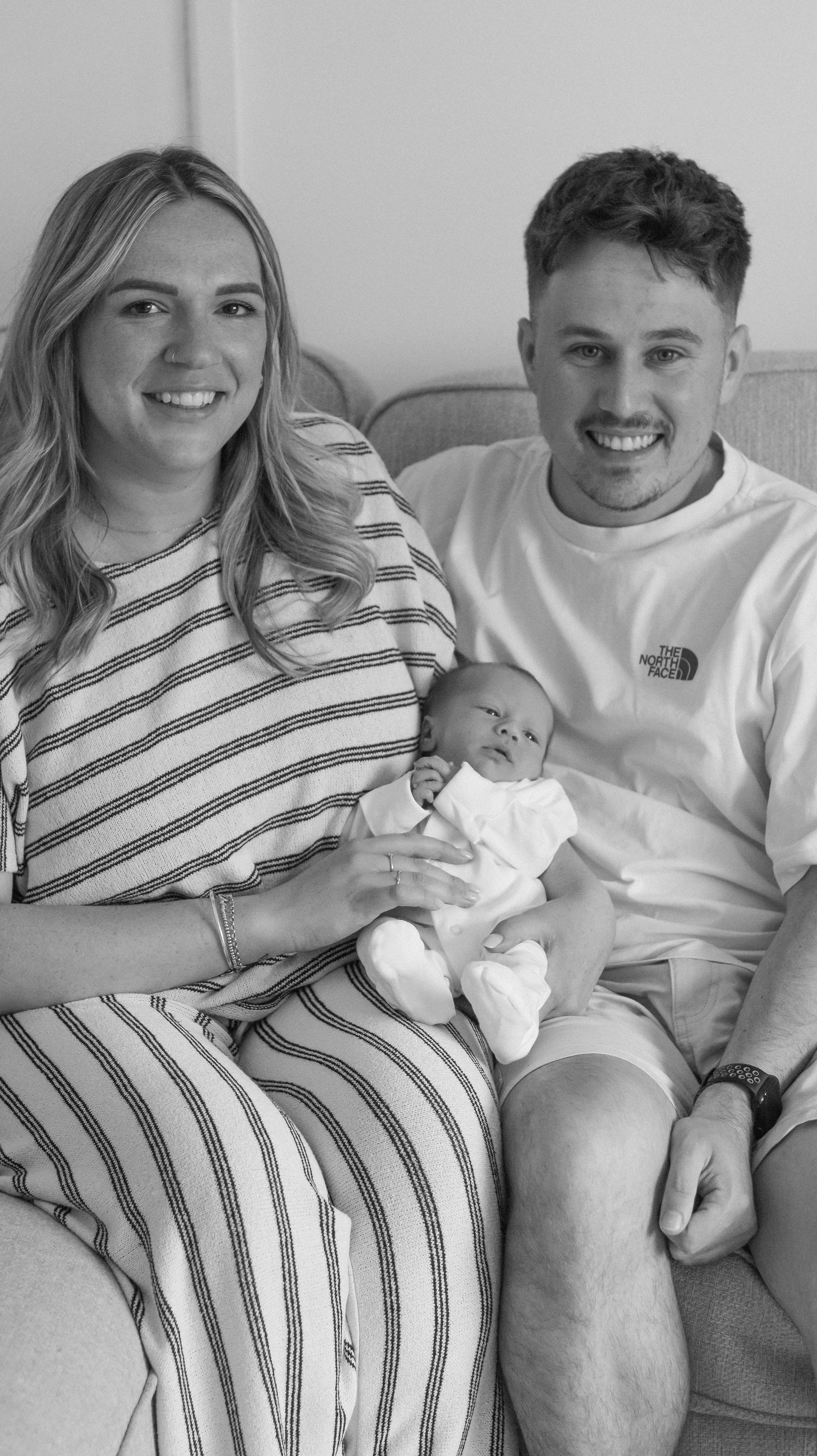 A happy family, including a woman, a man, and a newborn baby, sitting on a couch together.