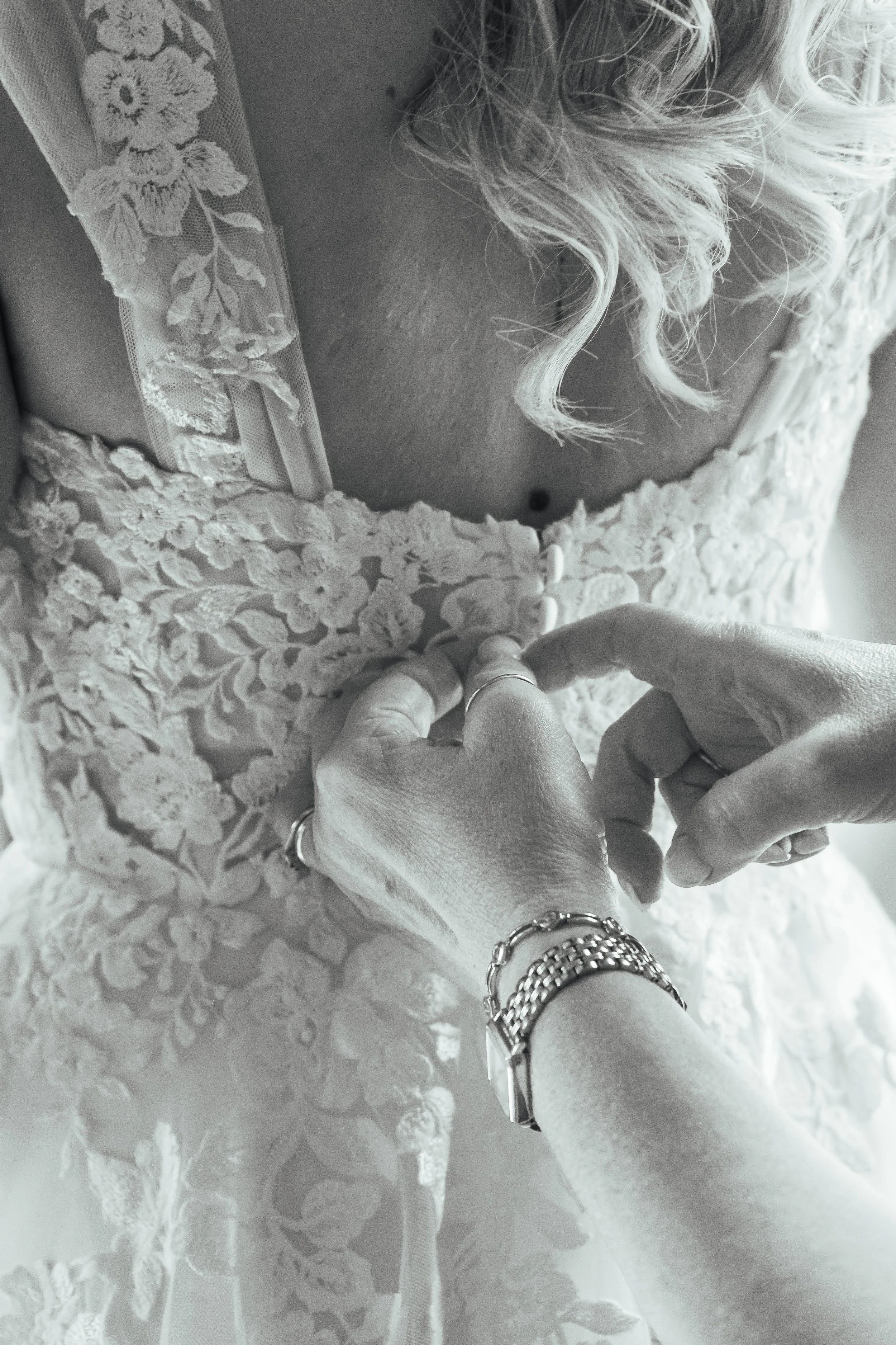 A woman is buttoning the back of her lace wedding dress.
