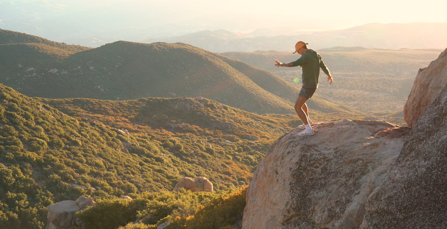 Isaak Rowe standing on a rock overlooking sunlit mountains