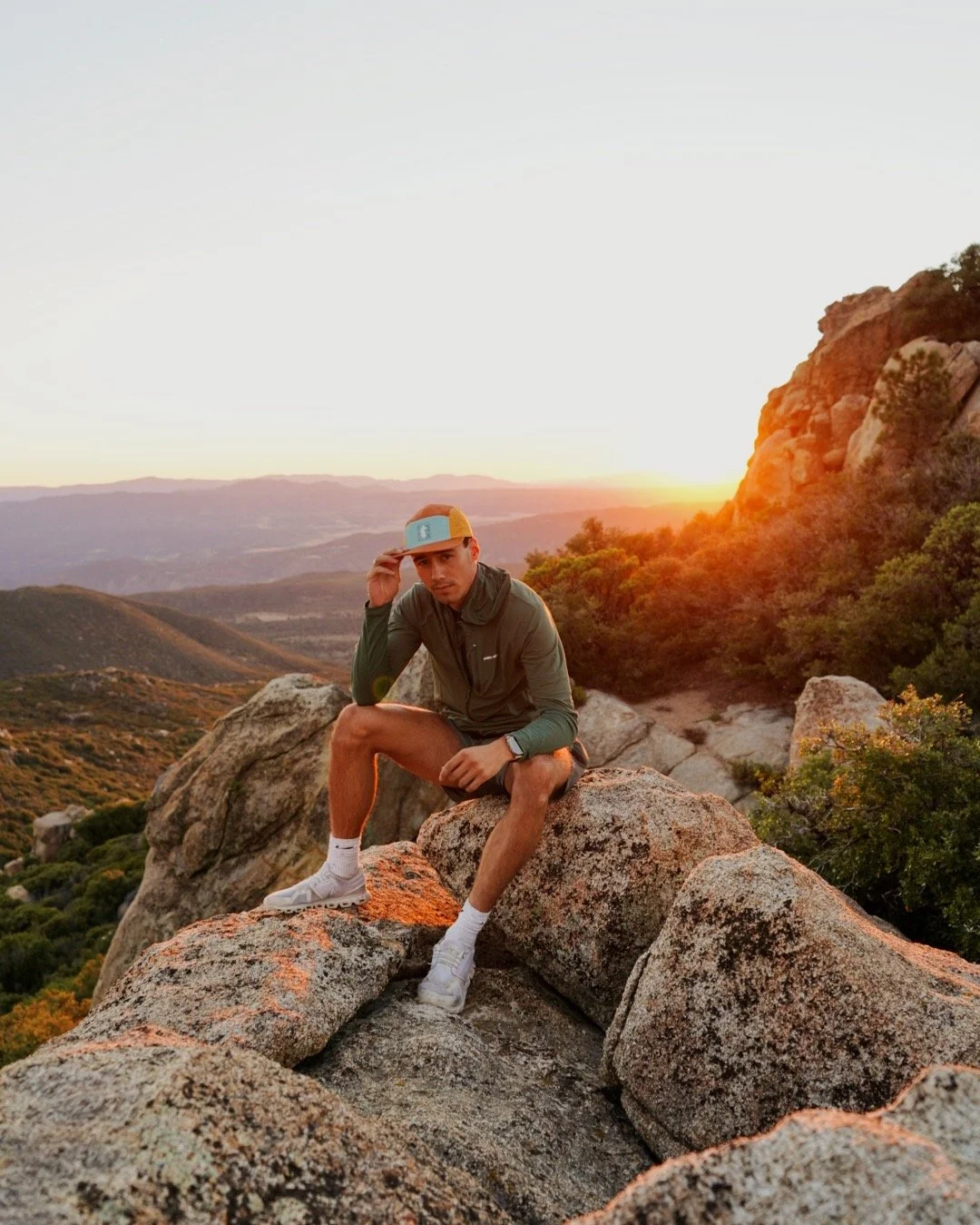 Isaak Rowe sitting on a sunlit rock in the mountains at sunset