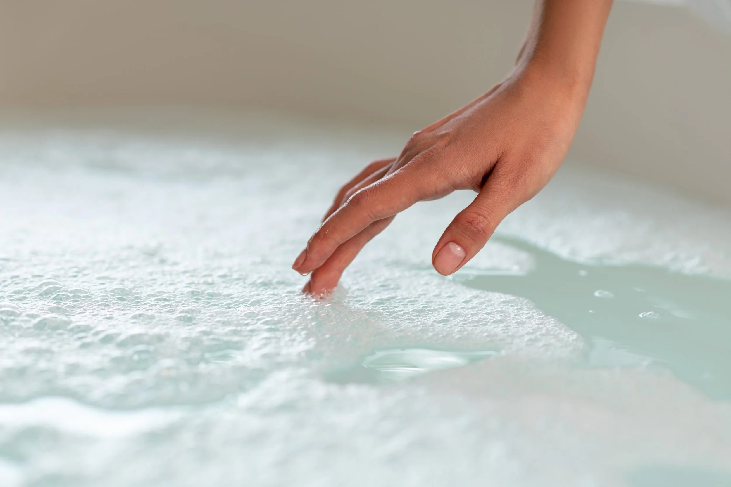 A hand touching the surface of soapy water, creating bubbles and foam.
