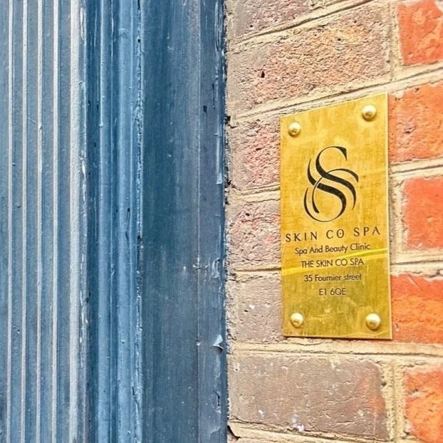 Gold sign for Skin Co Spa and Beauty Clinic mounted on a brick wall next to a blue metal door.
