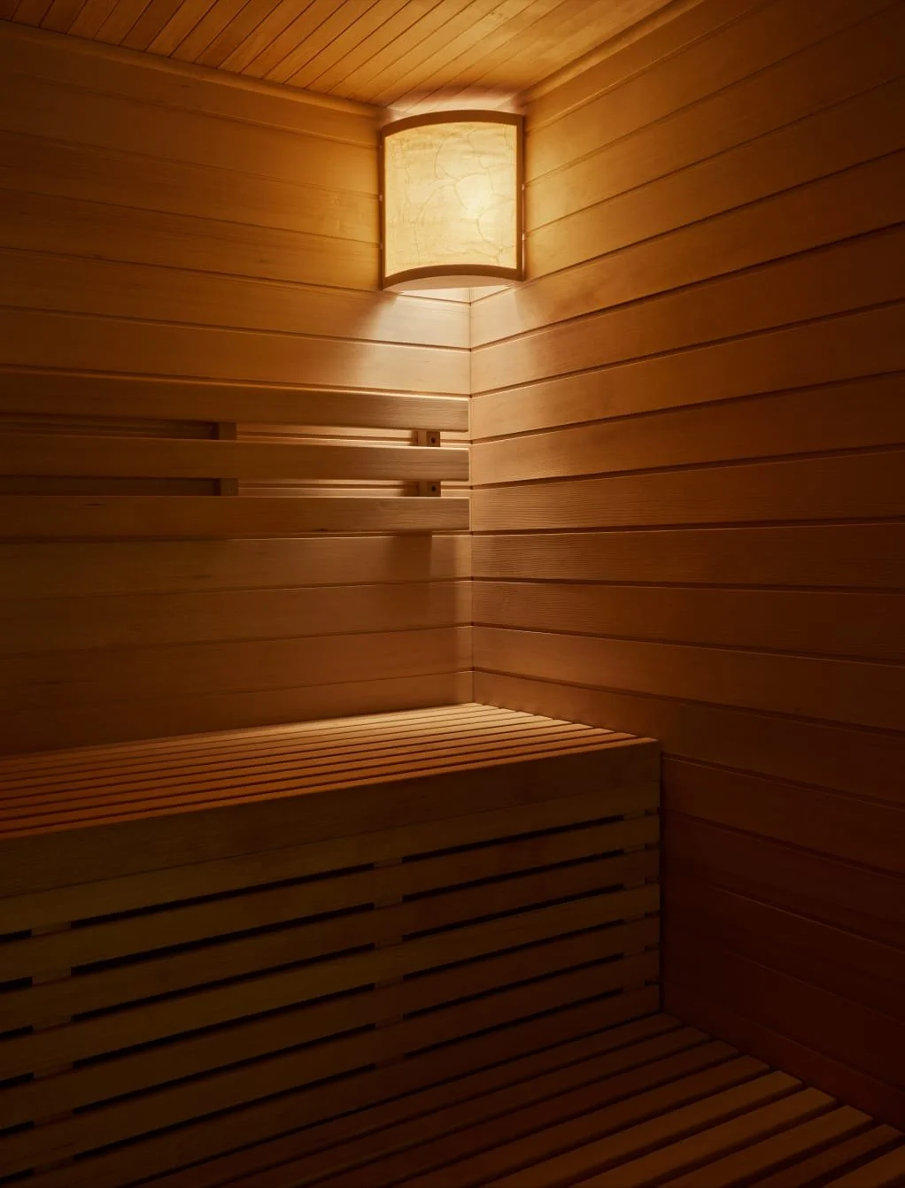 Wood-paneled sauna with a bench and a wall-mounted light fixture.