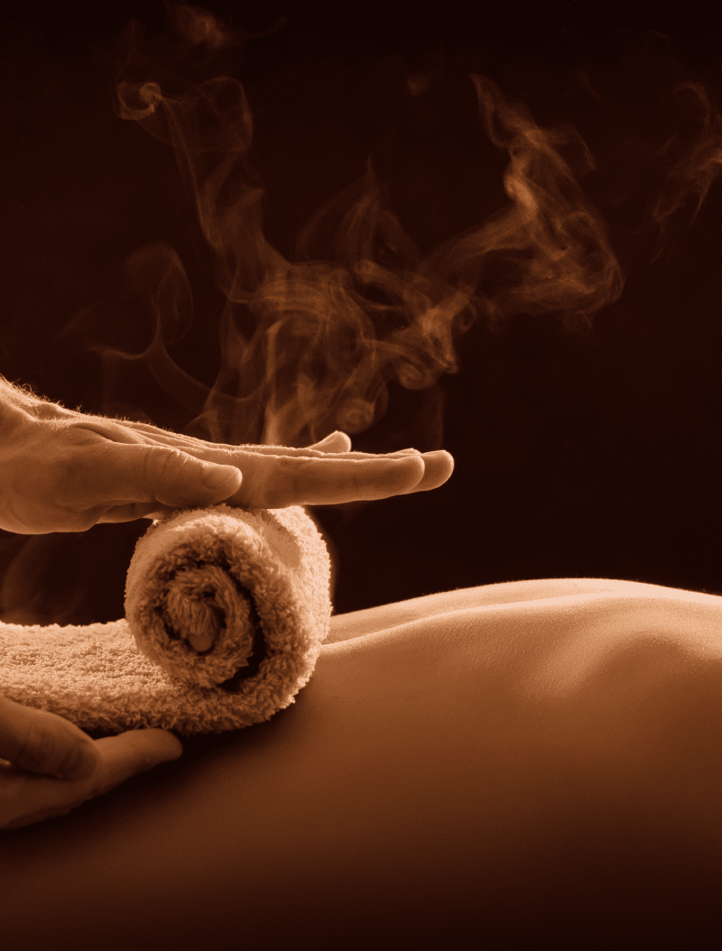 Close-up of a person receiving a massage with an aromatic rolled towel, warm steam rising, and a soothing ambiance.