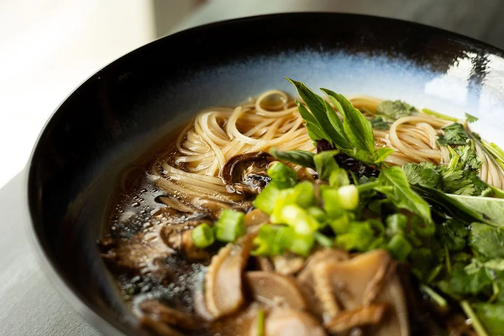  Close up of a bowl on ramen wiht noodles, shitakii mushrooms, and herbs in a broth 