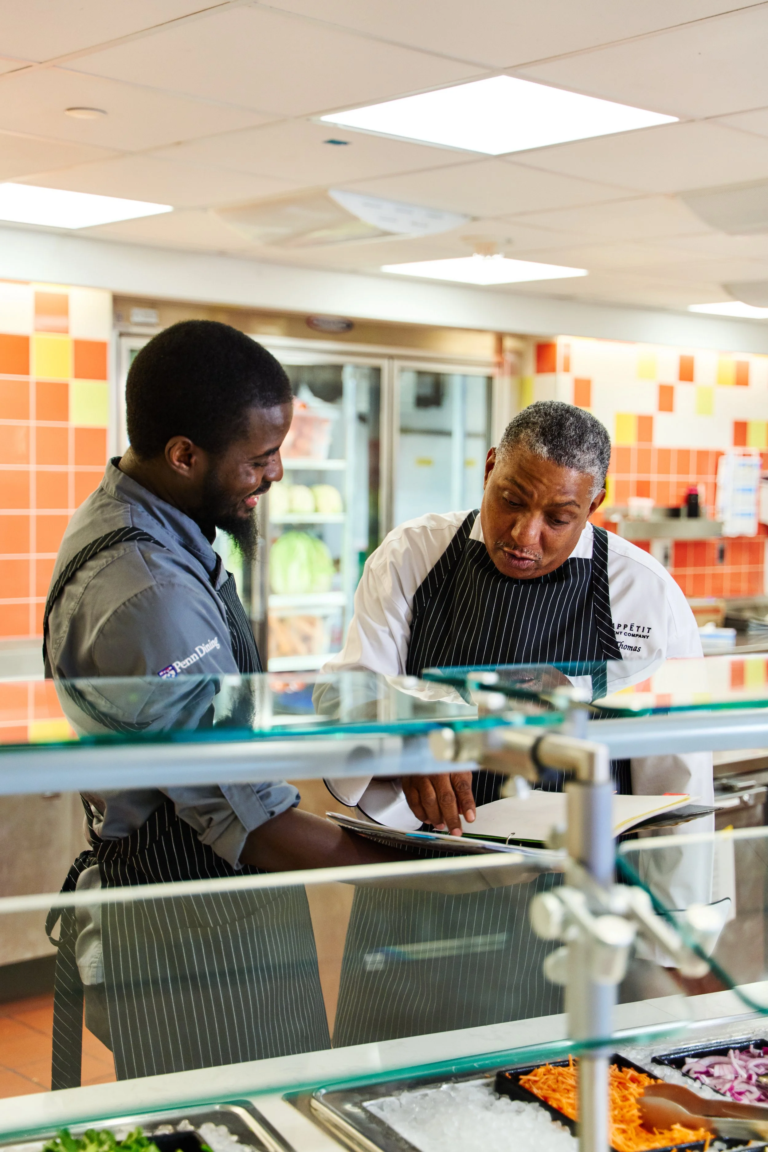  Two Bon Appetit employees review a binder while standing in front of the buffet bar 