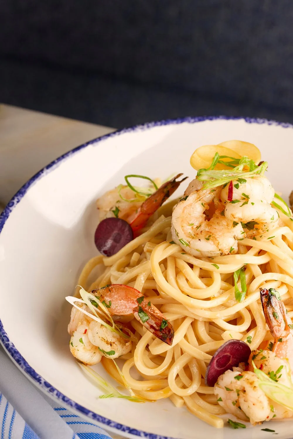 Close-up of a white bowl containing garlic noodles with grilled shrimp from the Noodle Bar slip in Farewinds Market Hall.