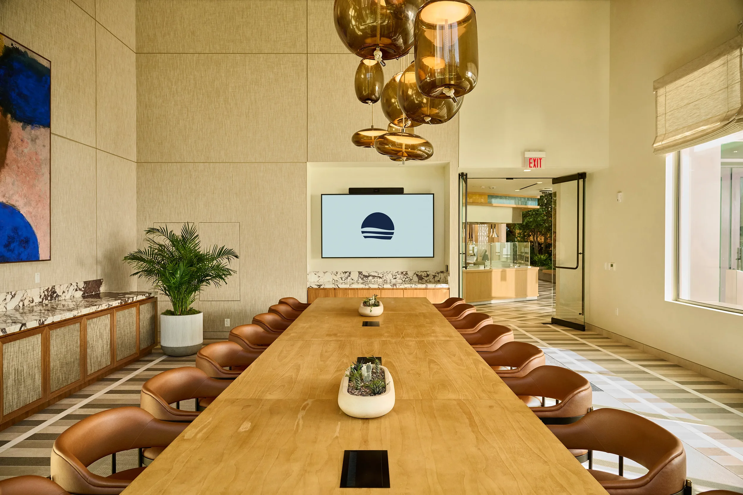 Reservable private dining room at Farewinds with long wooden table, brown chairs, abstract glass pendant lights, and 85-inch TV monitor mounted on the wall.