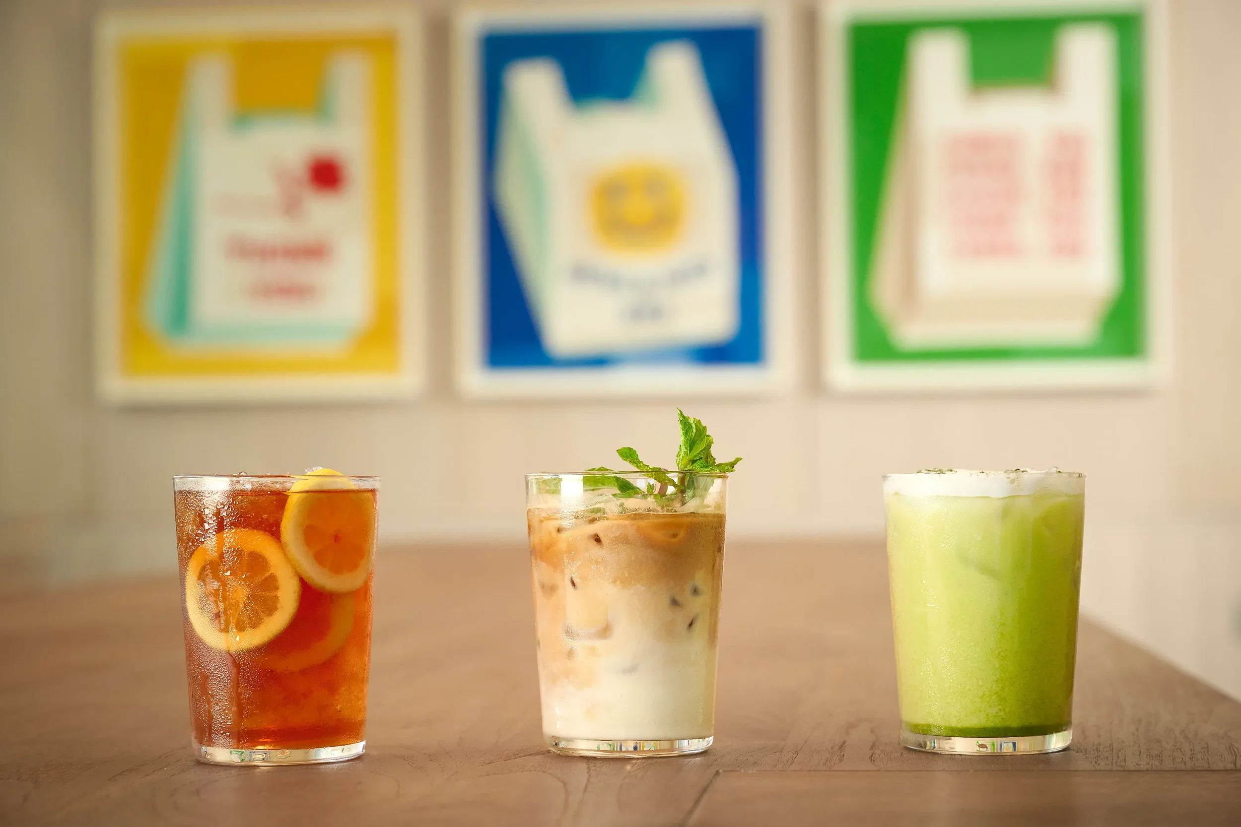 Three frosty iced beverages on a wooden table in Farewinds Market with colorful artwork in the background.