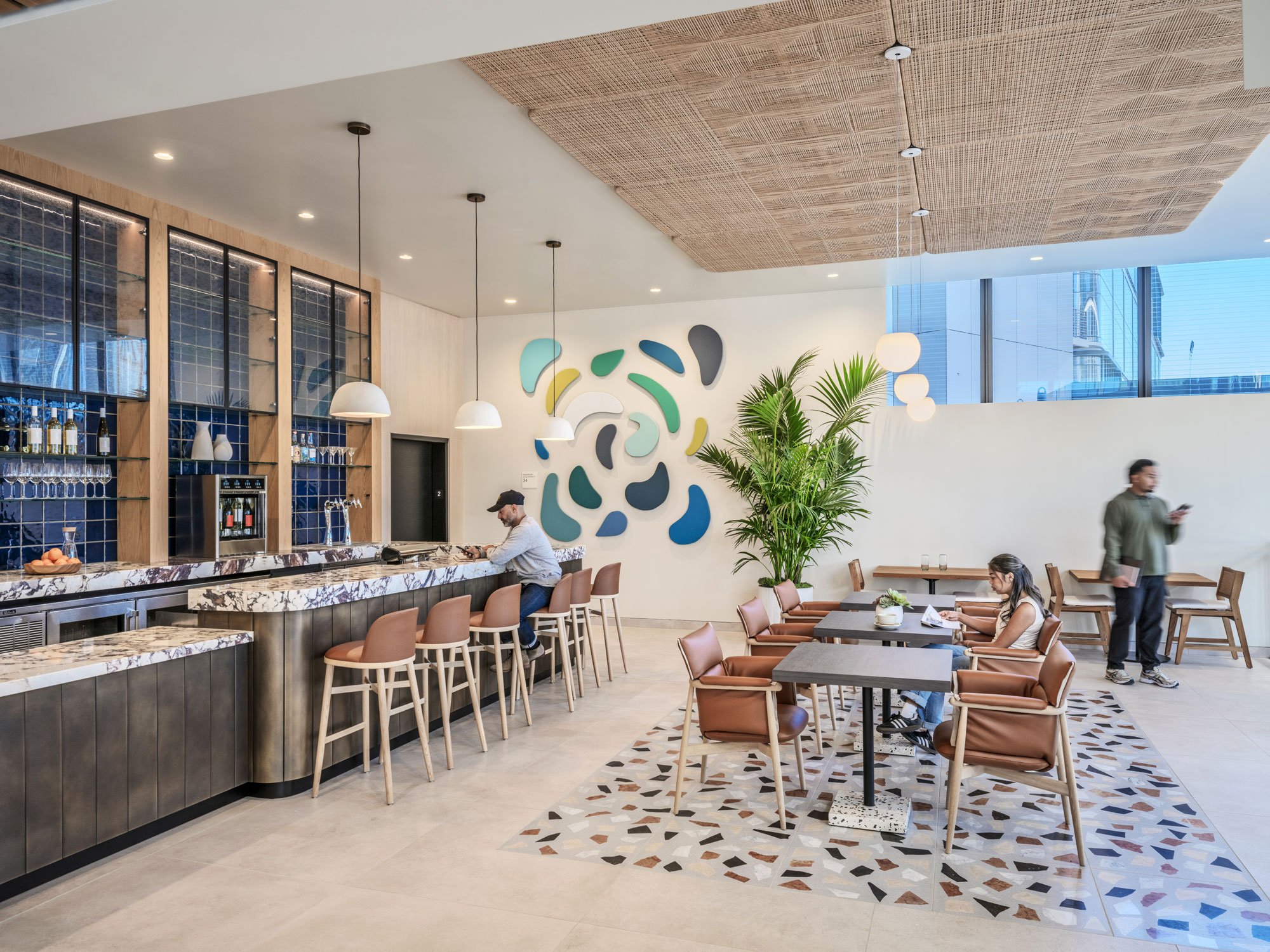 Customers sitting at the bar and a table in the cenral bar at Farewinds with a large plant and abstract colorful art on the wall.