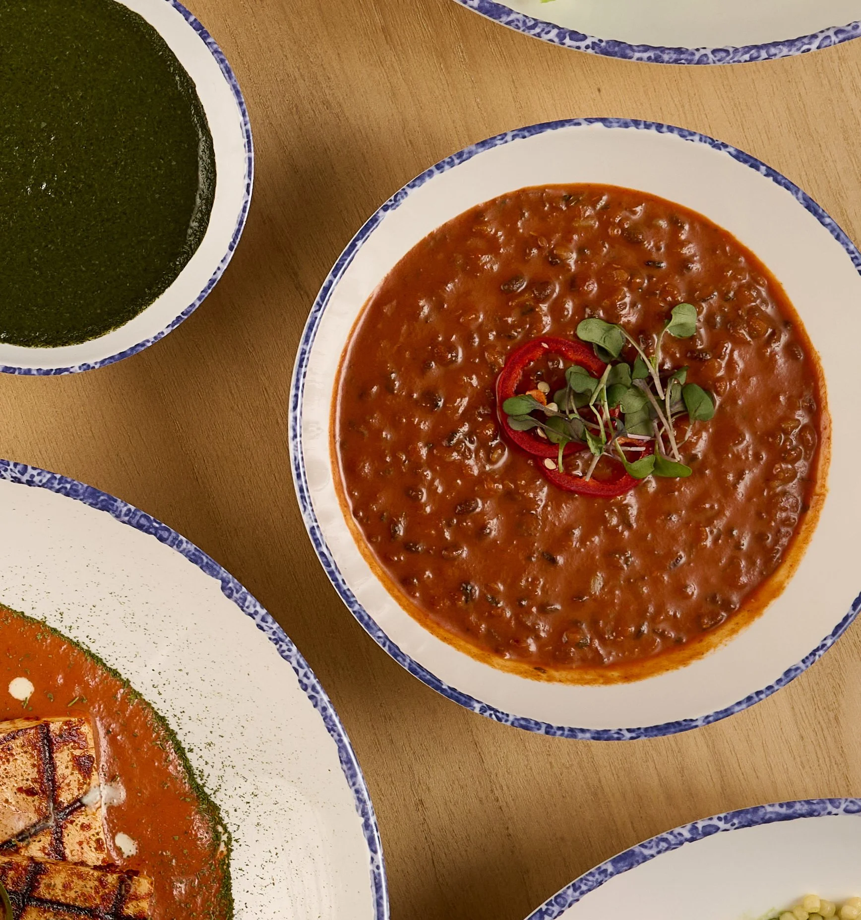 Overhead view of a white bowl with braised black urad, butter lentils, and kidney beans from the Indian slip in Farewinds Market Hall.