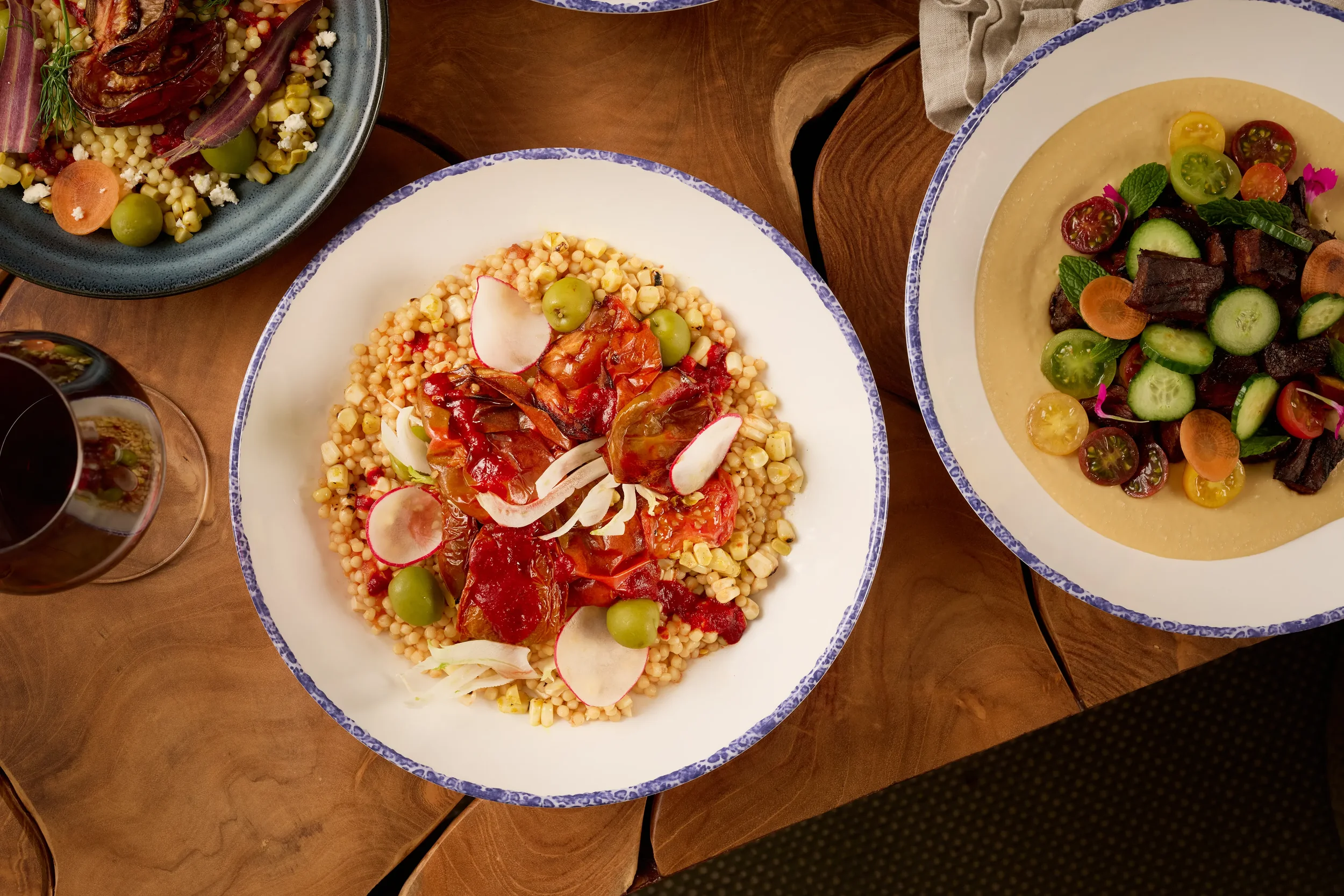 Two white plates, one with charred tomato couscous and the other with a steak and hummus plate from Mezza in Farewinds Food Hall.
