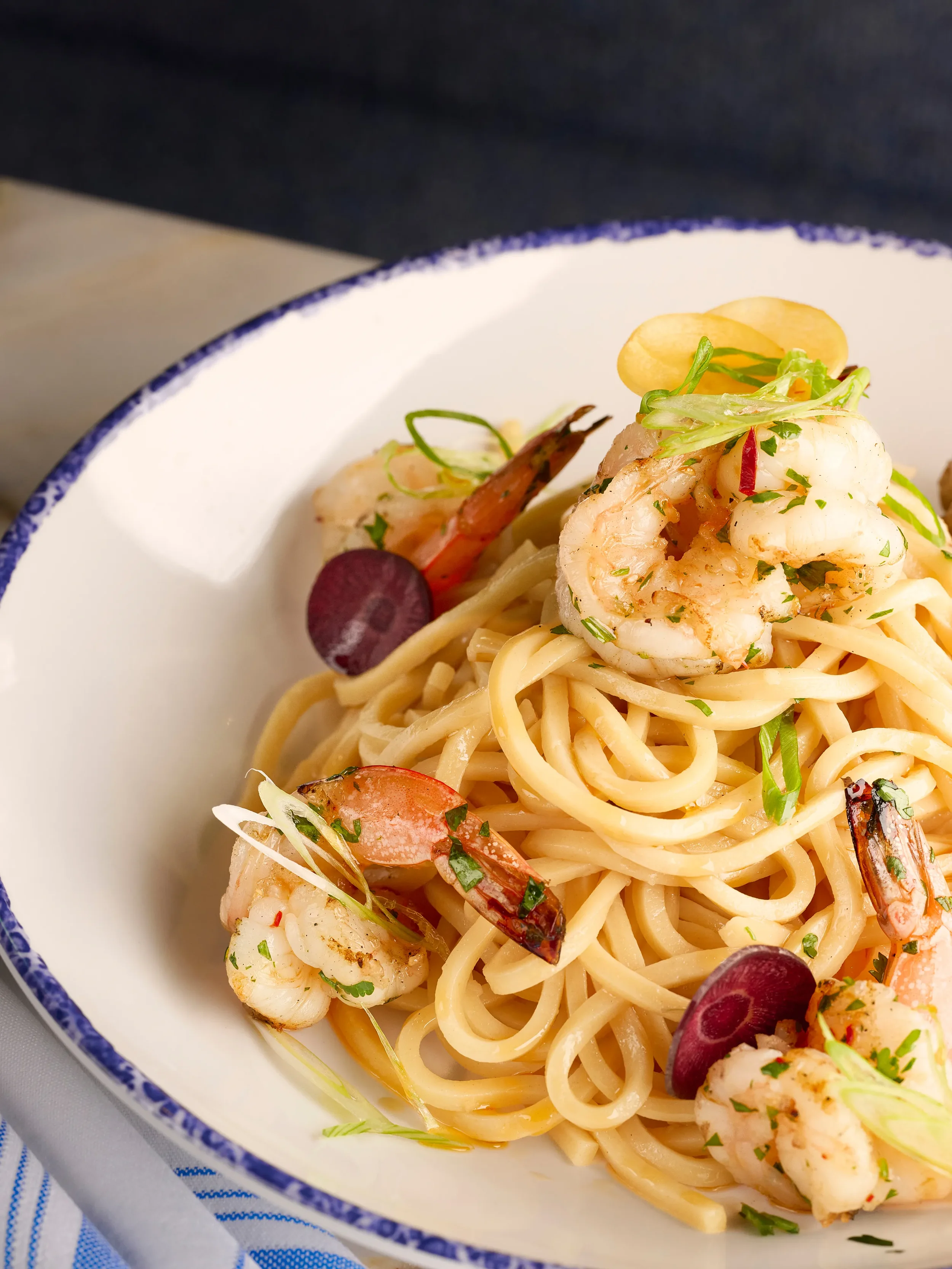 Close-up of a white bowl containing garlic noodles with grilled shrimp from the Noodle Bar slip in Farewinds Food Hall.