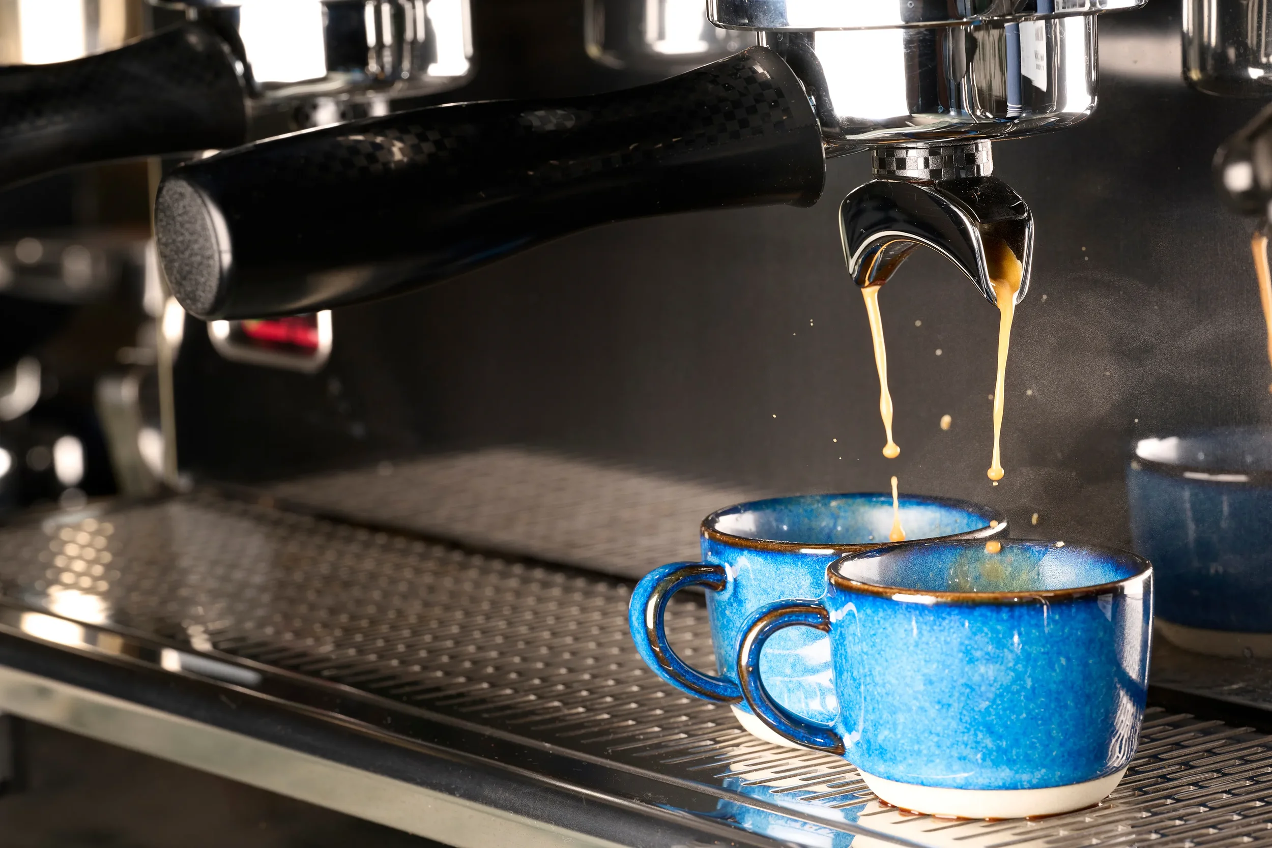 Pulled espresso dripping from a double-spouted portafilter into two blue ceramic cups.
