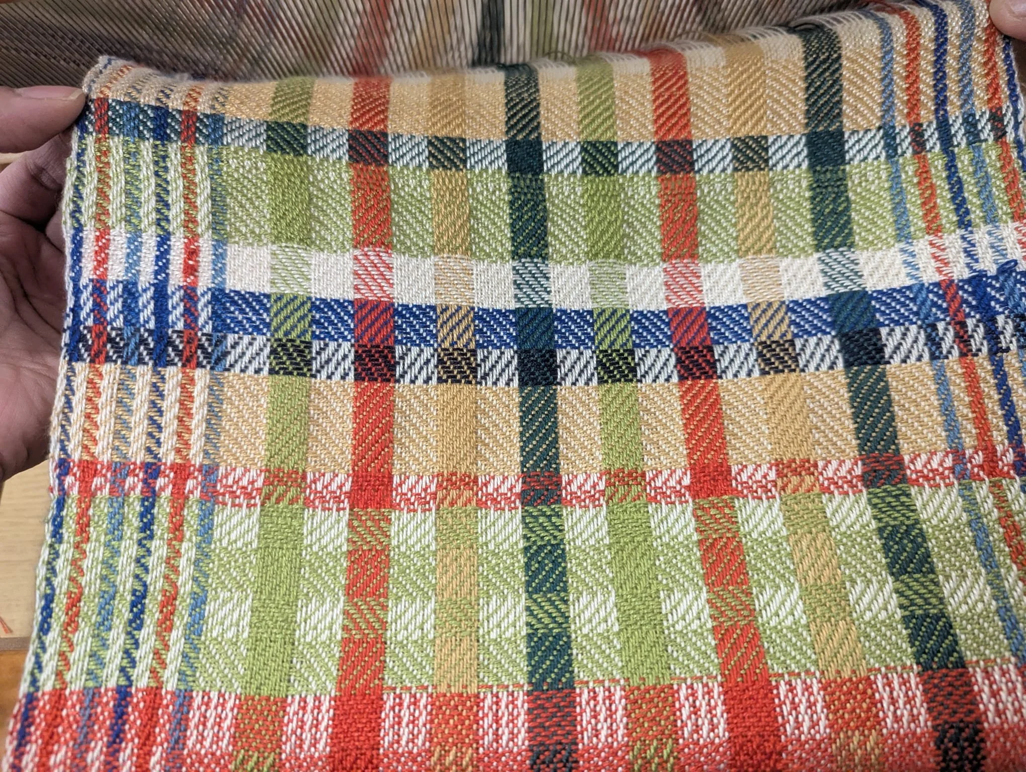 Close-up of a hand holding a colorful tartan-patterned fabric with red, green, white, blue, and black checks.